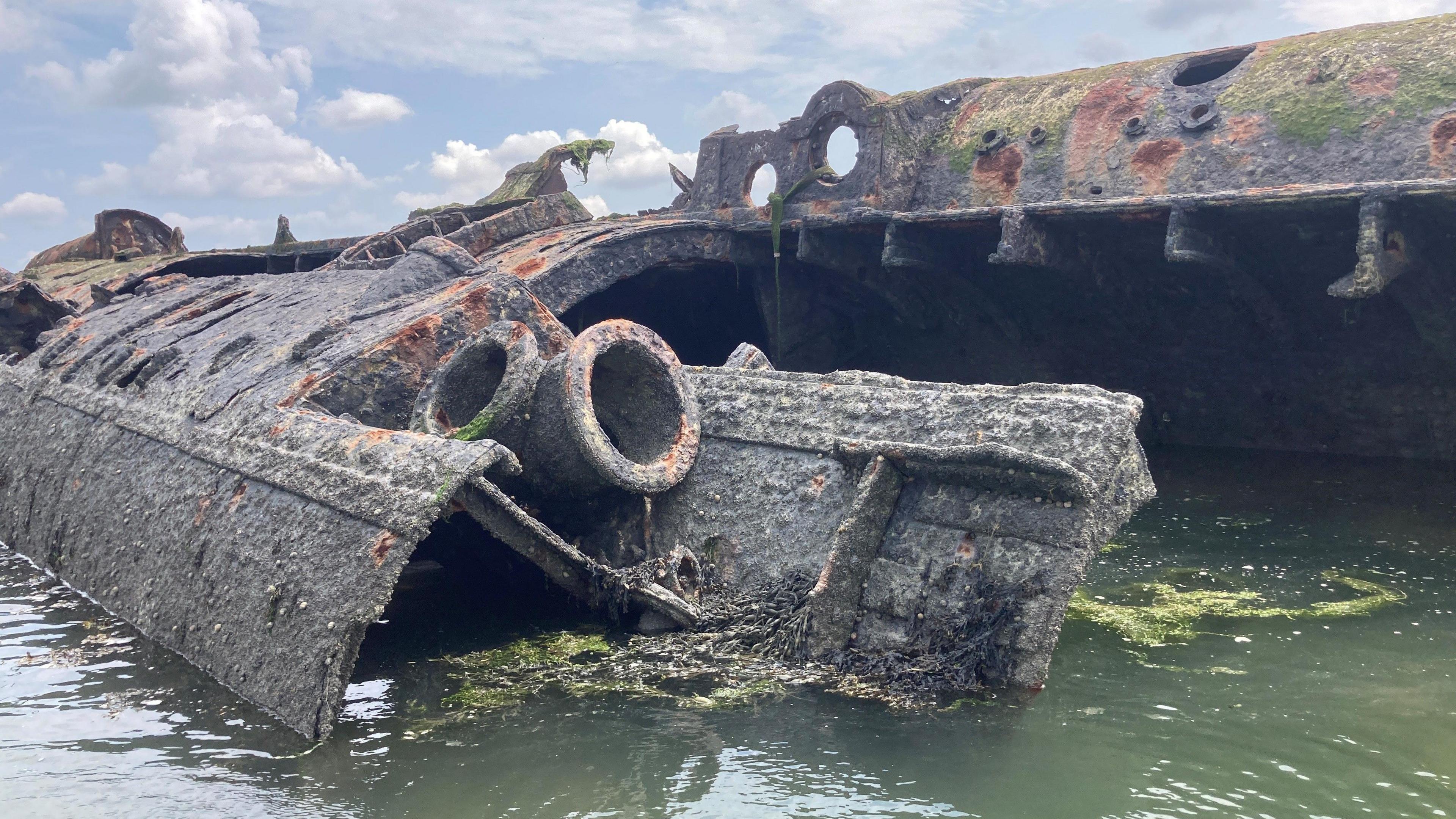 A green, grey and red rusting wreck of a German U-boat lies in green water.