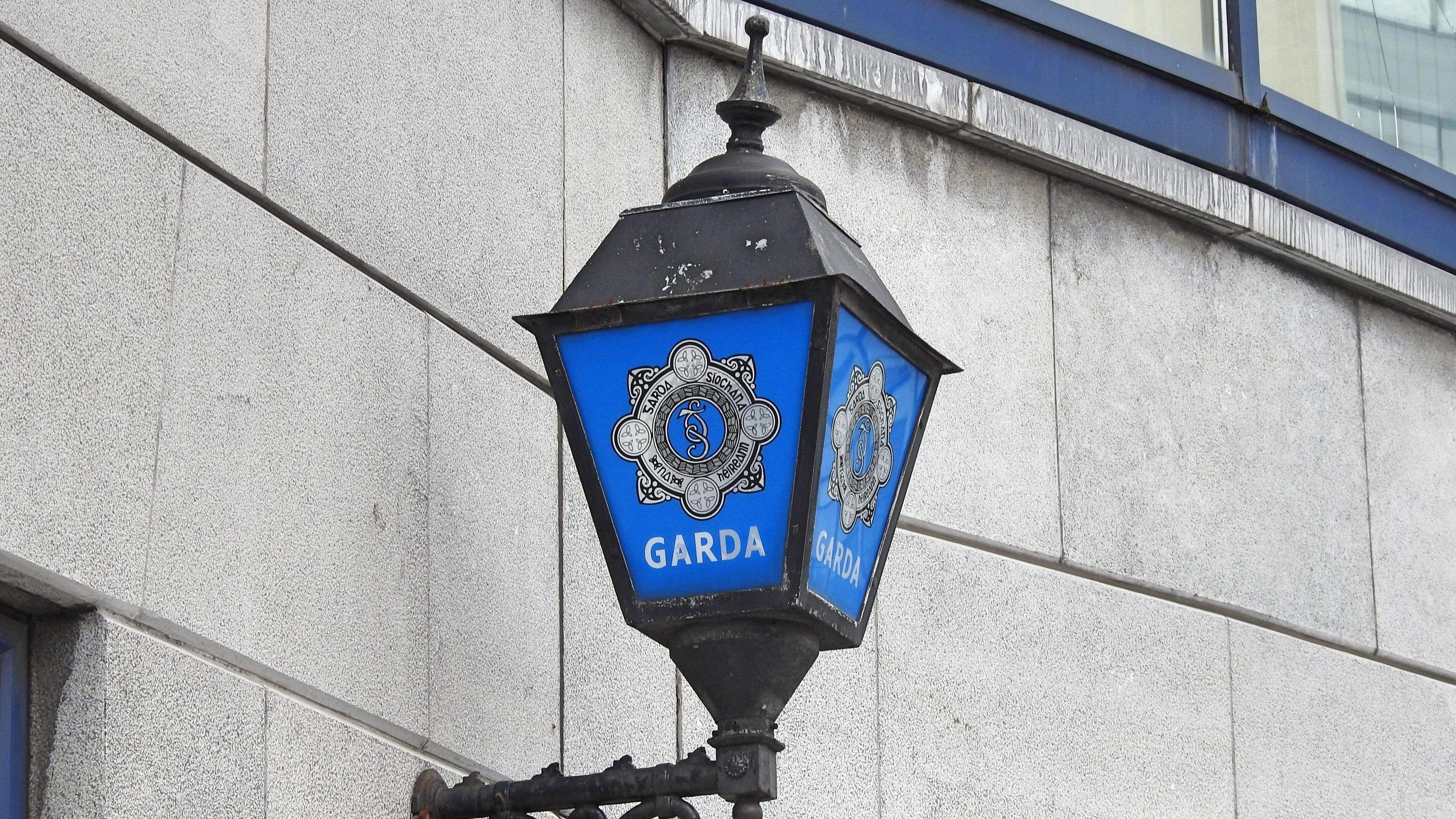 A close up of a lantern outside a garda station. The gardaí logo is on the lantern, which is attached to a grey brick wall.
