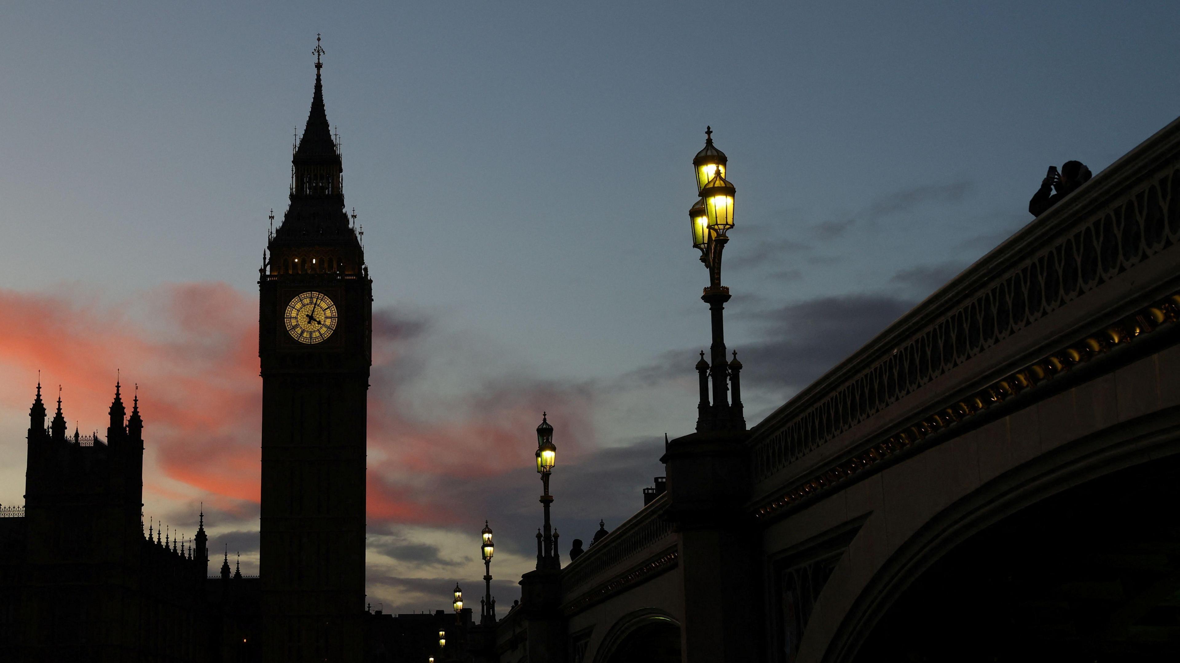 Elizabeth Tower, more commonly known as Big Ben, and the Houses of Parliament at dusk. The buildings are seen in silhouette, but the clock face is lit up. 