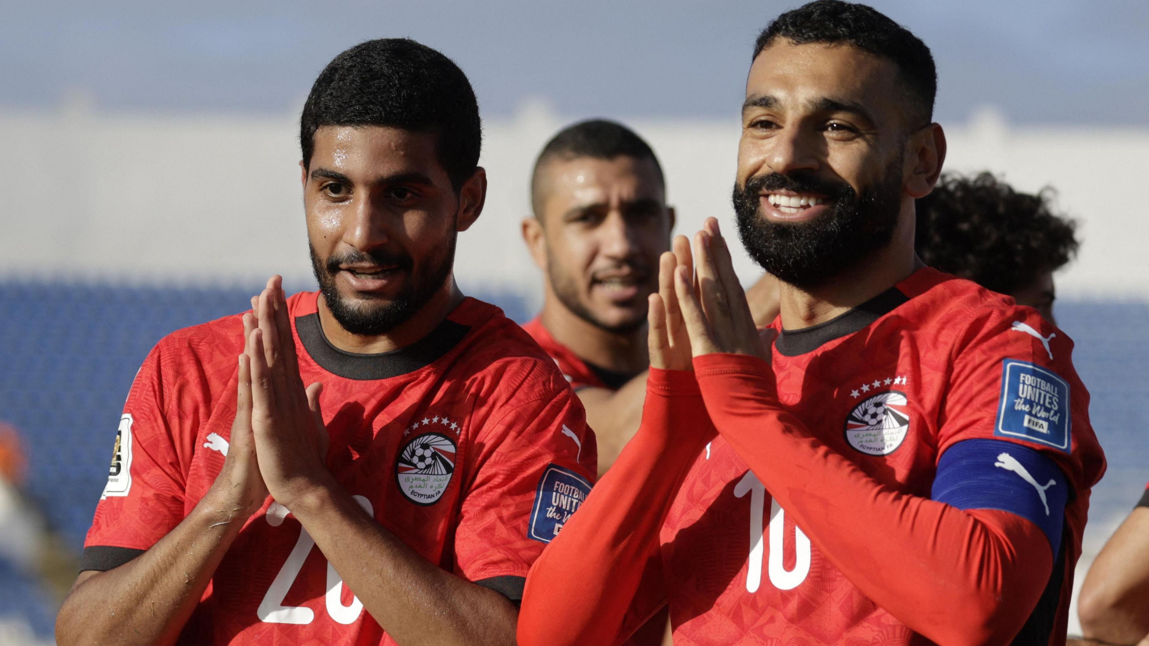 Ibrahim Adel and Mohamed Salah, both wearing red Egypt football shirts, put their hands together in a prayer position as they