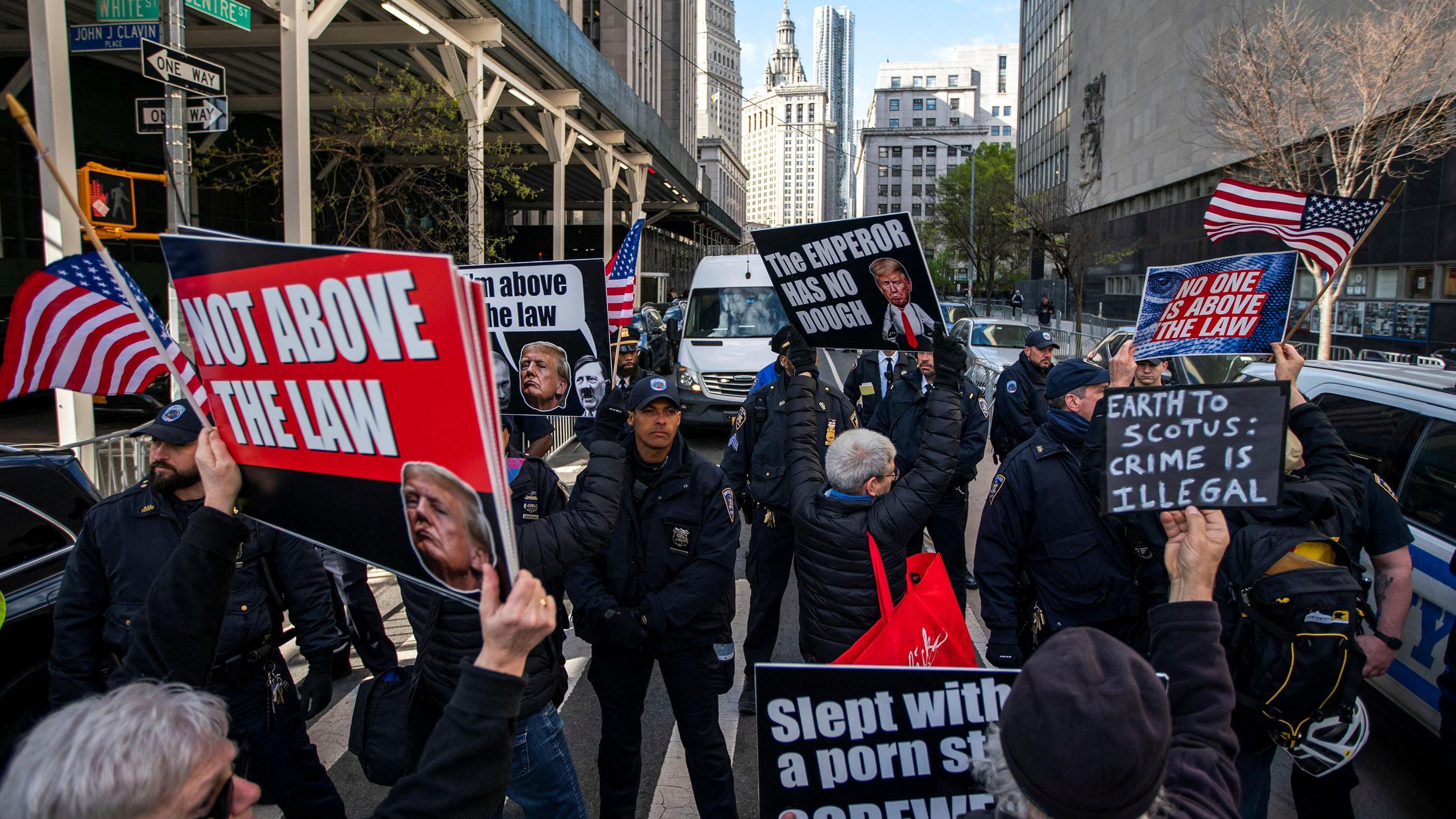 Protests hold signs reading "not above the law" and the "the emperor has no dough"  as police stop them from approaching the Manhattan criminal court