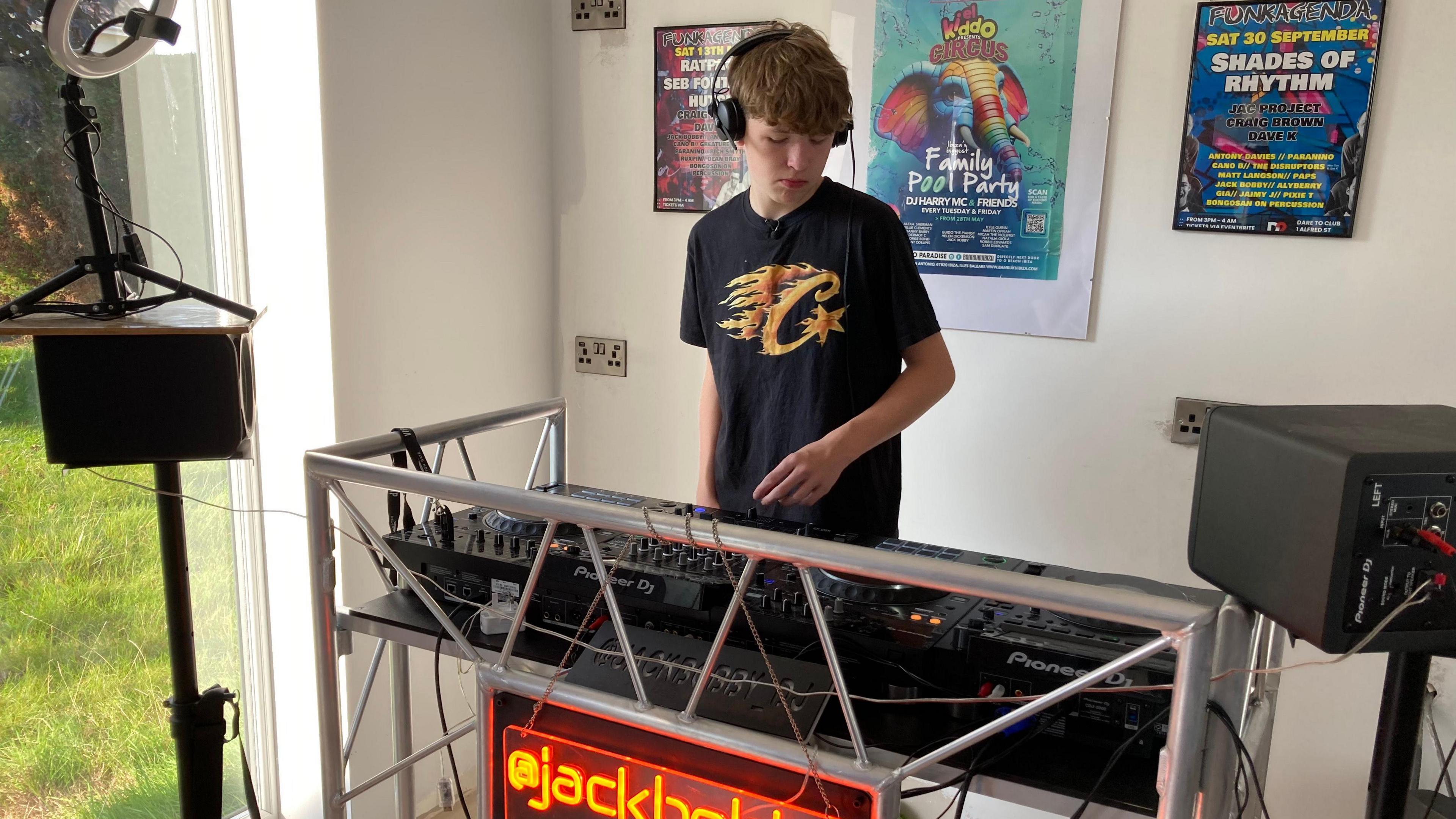 Jack Bobby standing in front of a pair of decks and speakers wearing, headphones and dark clothes