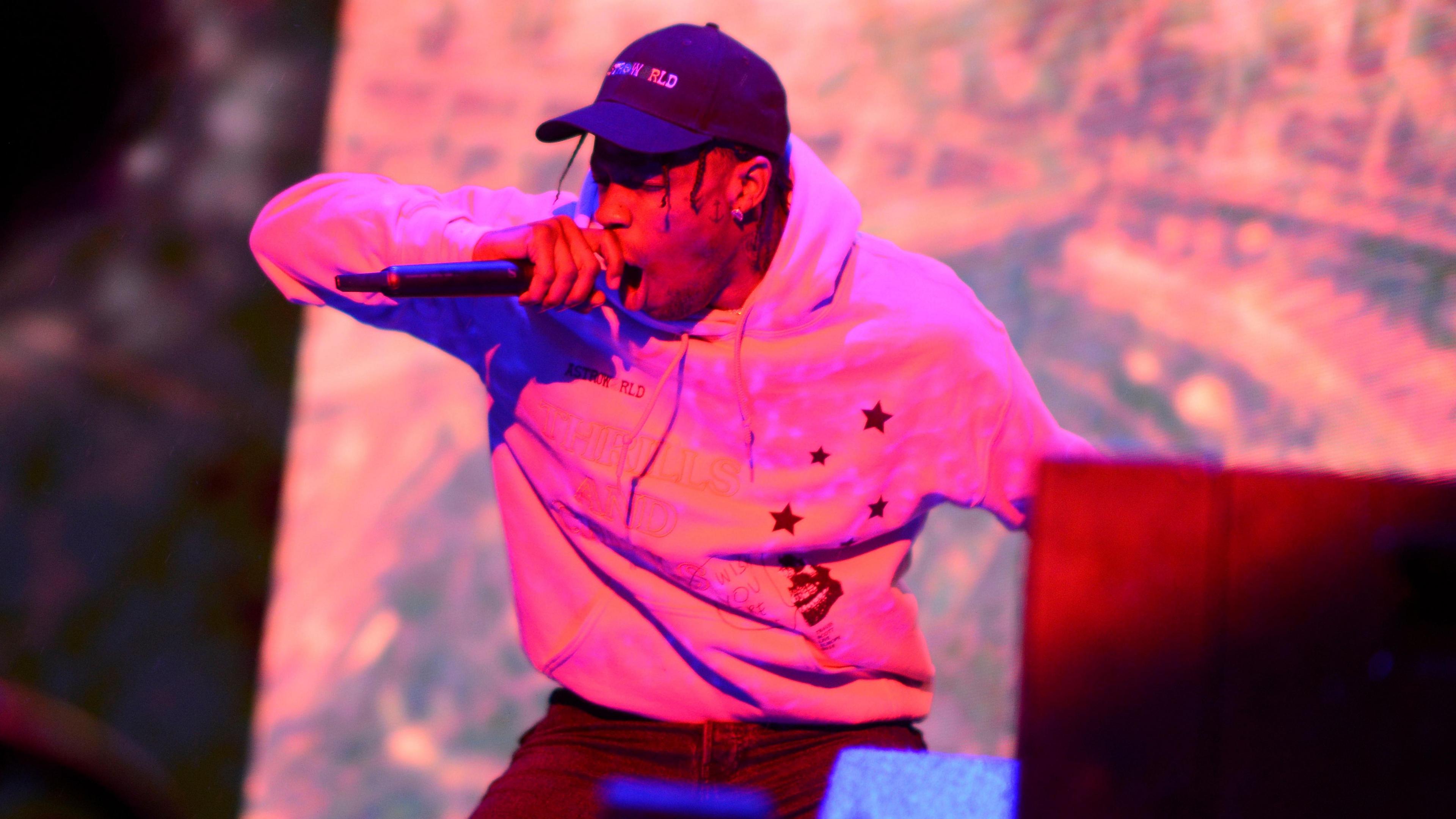 Travis Scott performing at Reading. He wears a cap, hoodie, and jeans.