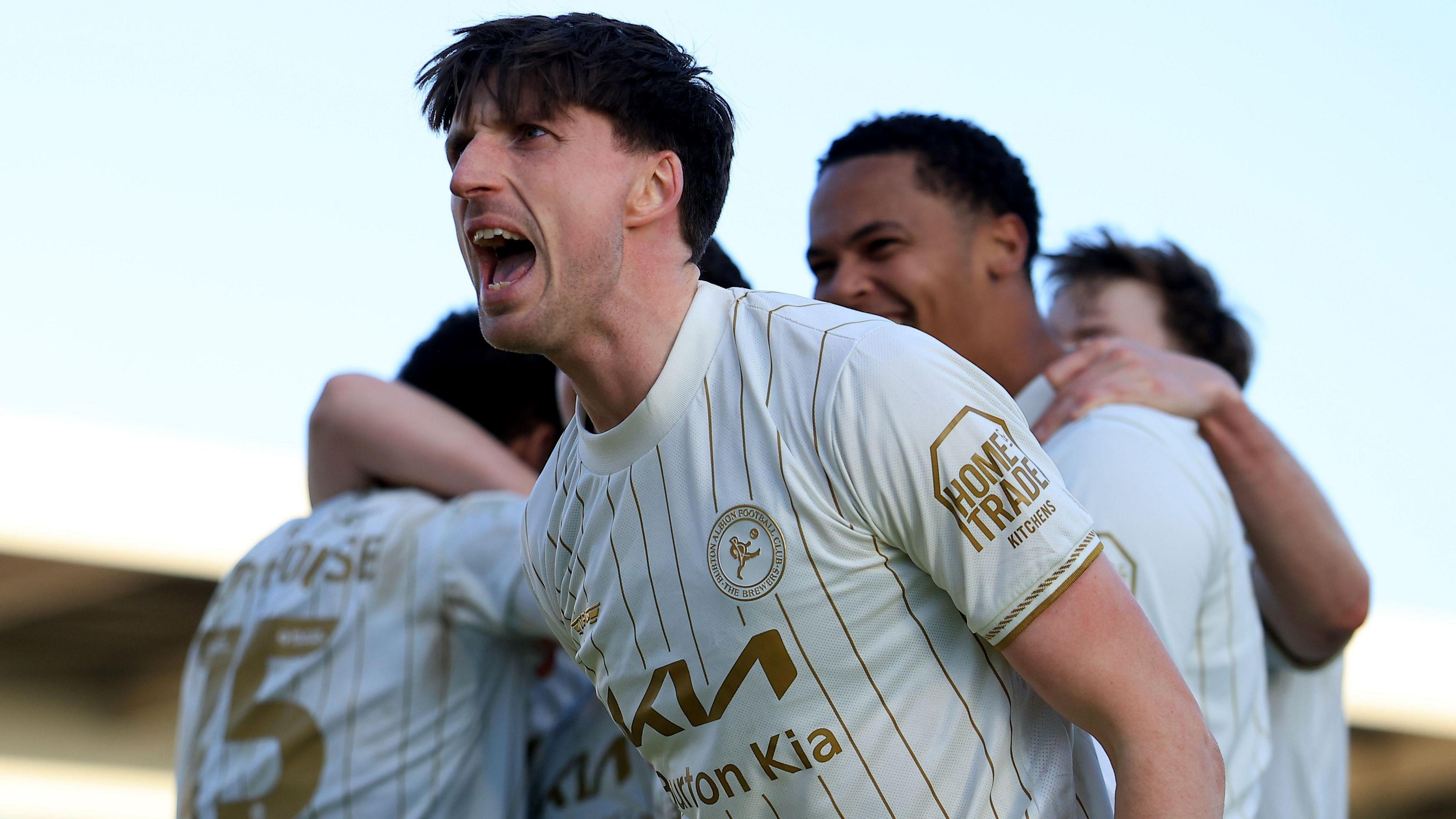 Jake Beesley, in Burton Albion's white change strip with gold pin stripes, celebrates with his team-mates at Northampton
