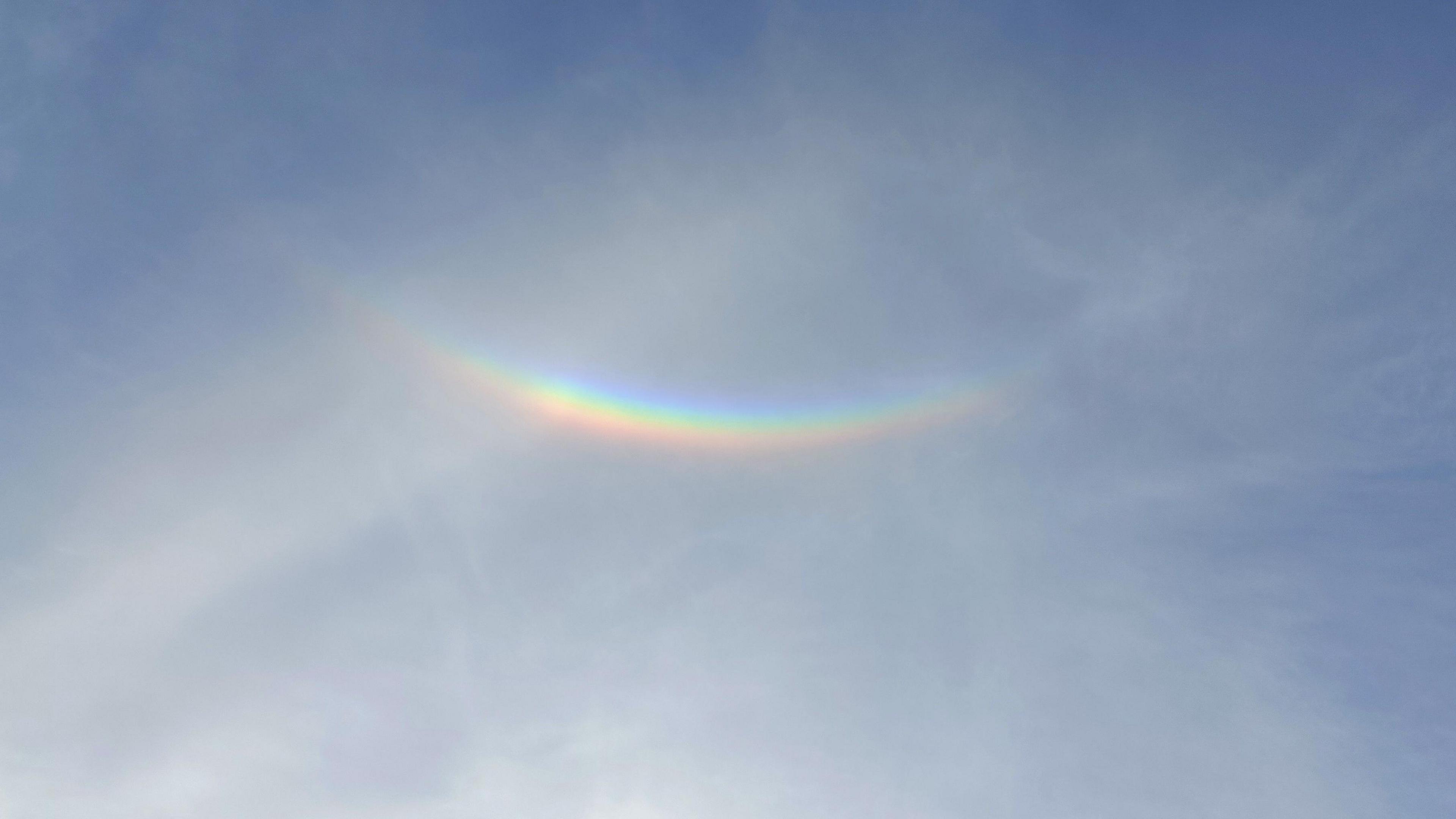 An upside down rainbow which is an optical illusion, seen against a blue sky with wisps of white clouds. 