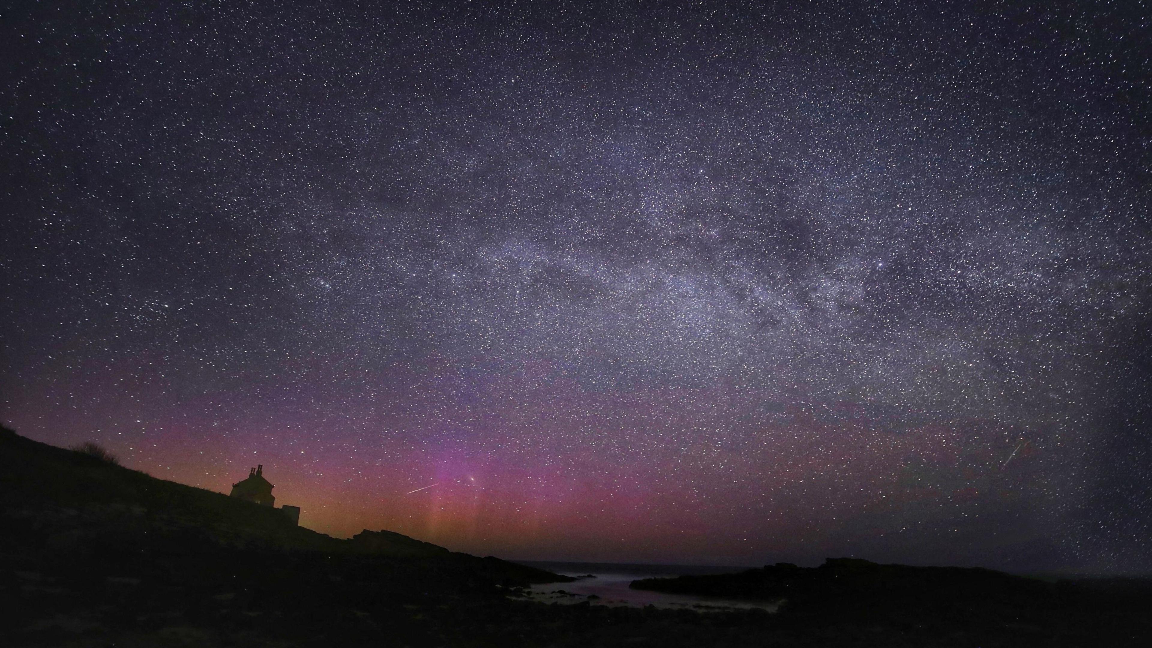 An expanse of nighttime  entity  implicit    a agrarian  landscape, showing the Northern Lights, the Milky Way and a meteor 