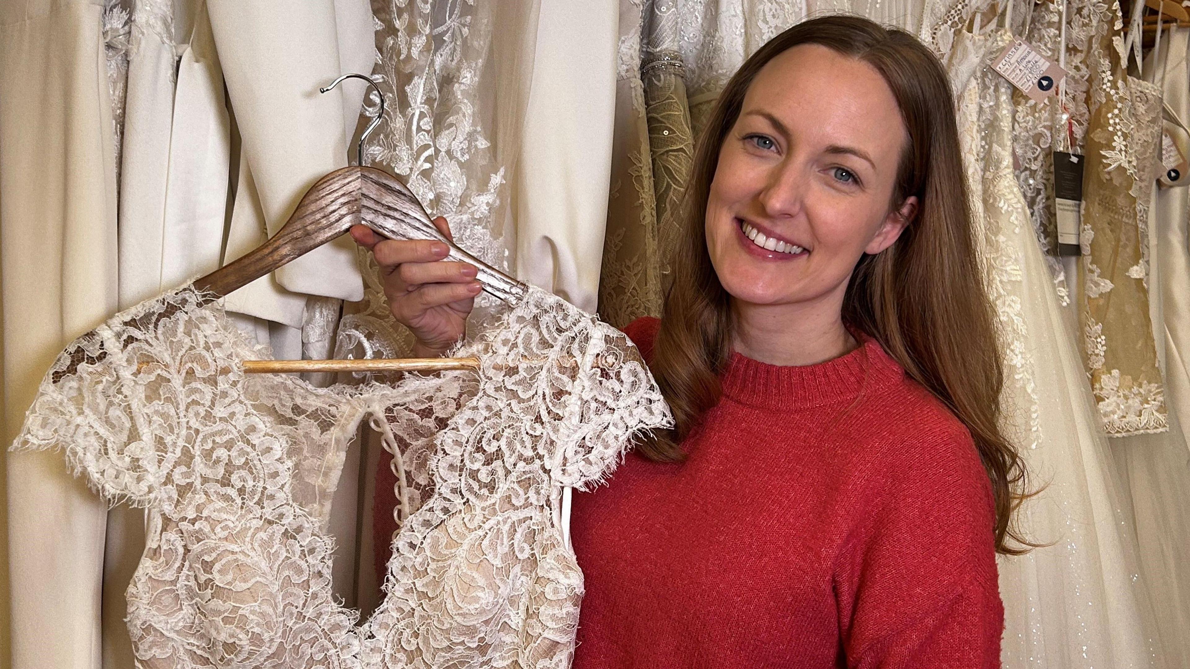 Mae Bronwen Barclay yn sefyll o flaen rhes o ffrogiau priodas. Mae ganddi wallt hir brown ac mae'n gwsgo siwmper goch. Mae'n dal ei ffrog briodas i fyny ac mae modd gweld ychydig ohoni. Mae'n ifori ac wedi ei gwneud o les, does dim llewys ar y wisg. 