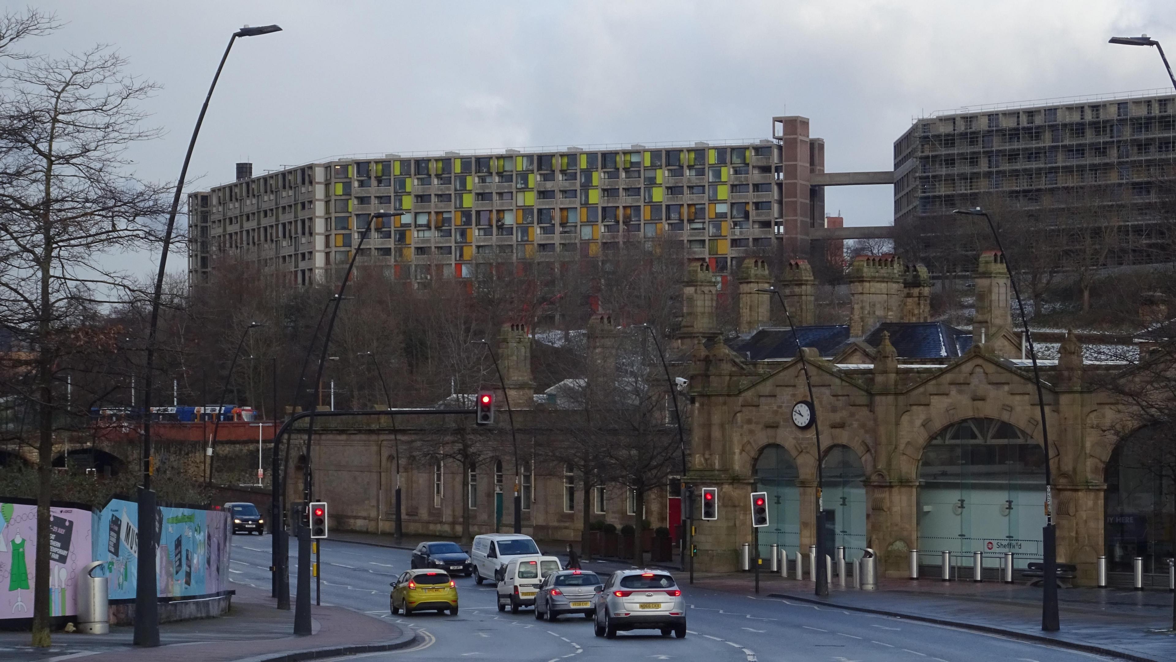 A large block of flats stands on the skyline as cars snake passed Sheffield railway station in the foreground