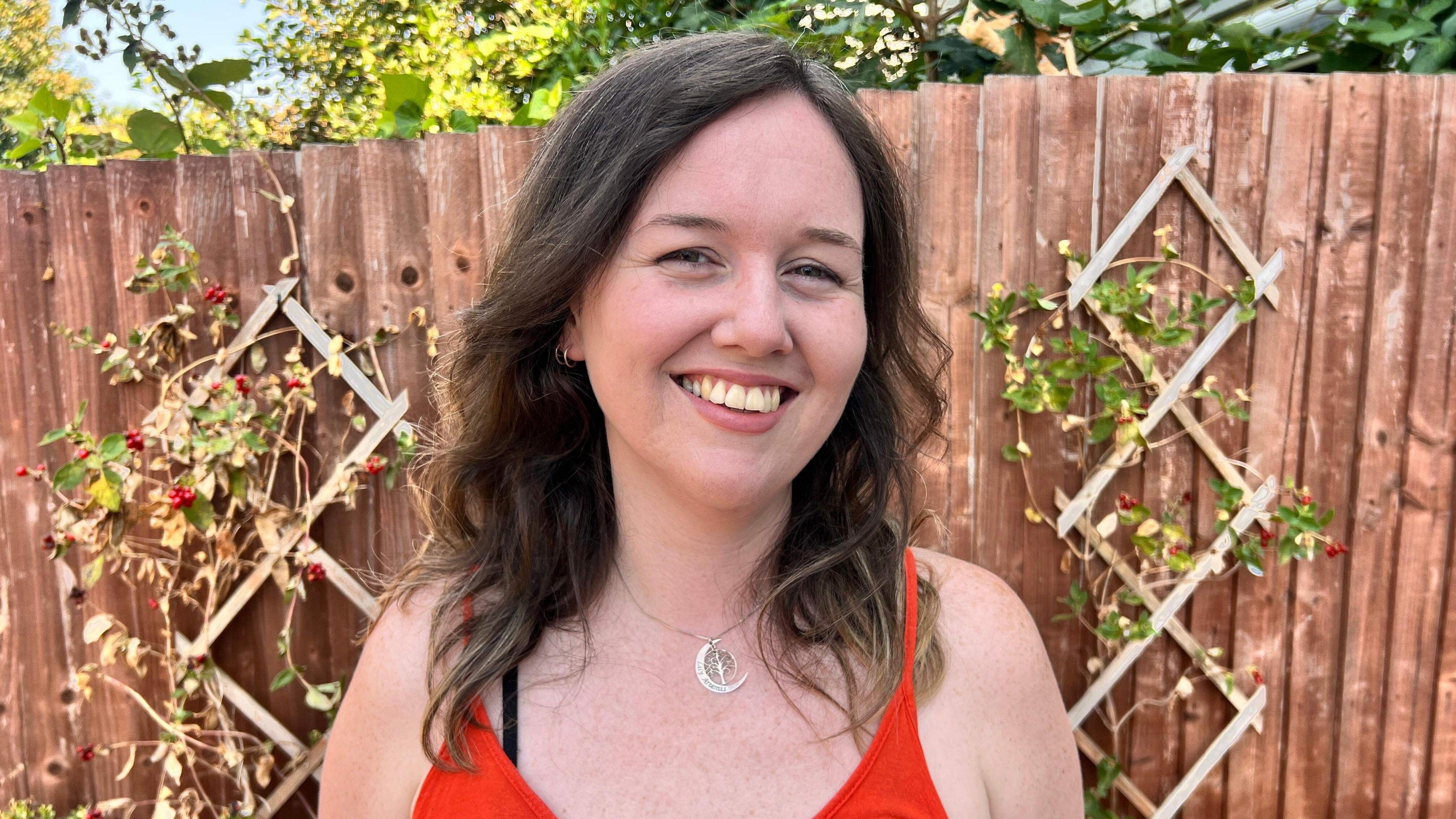 A white woman with brown hair smiles in the garden looking at the camera.