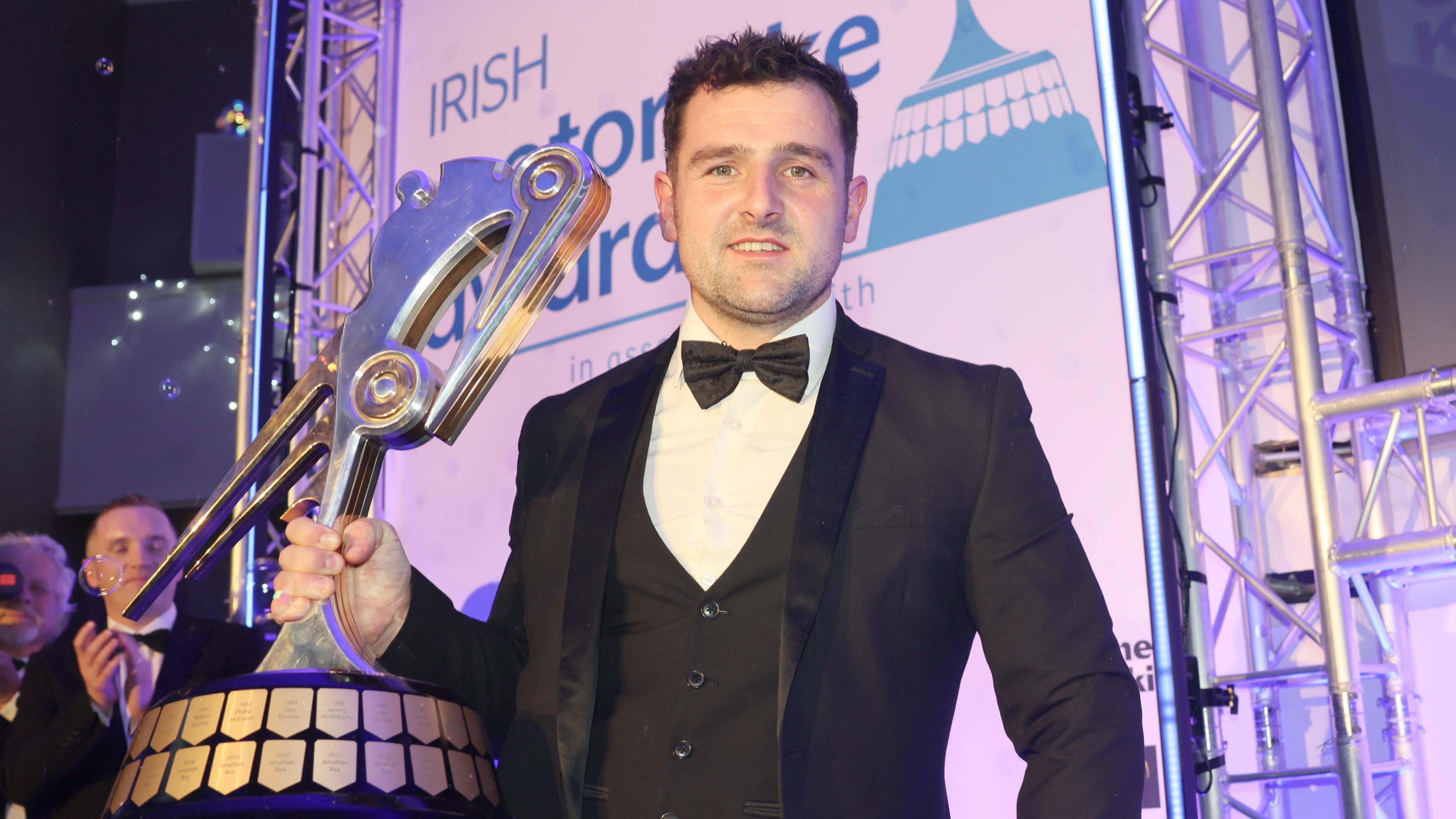 Michael Dunlop accepting the Joey Dunlop Trophy at a formal awards ceremony, dressed in a suit.