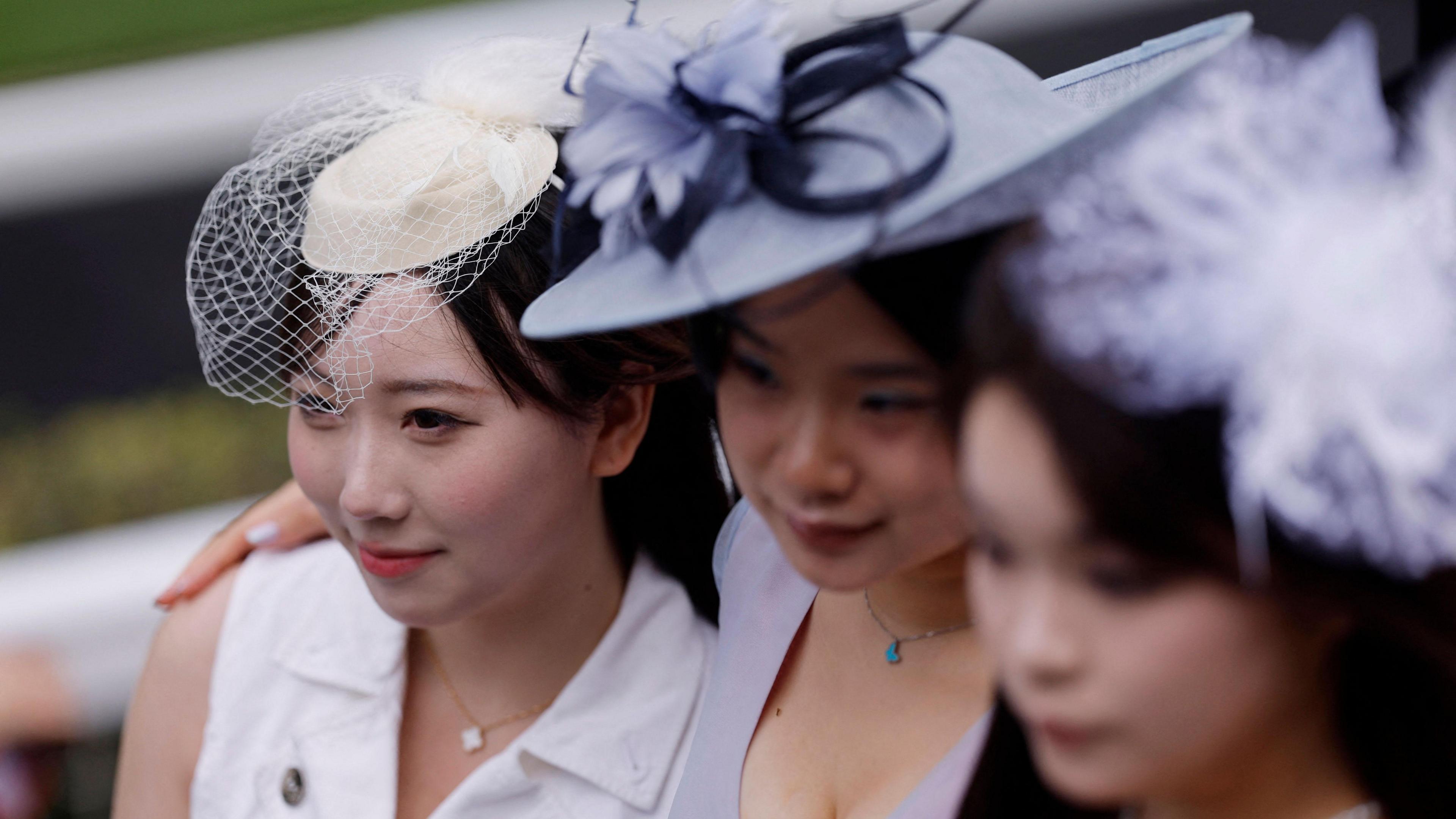 Three young woman with elegant hats on, with their arms round each other, smiling