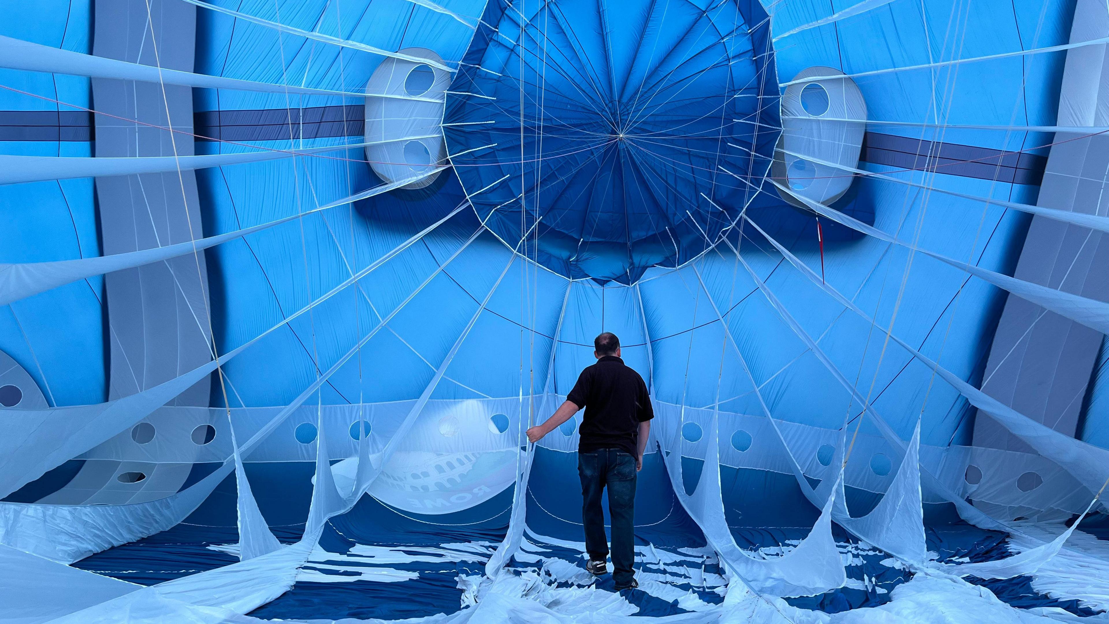 The inside of a big blue and white hot air balloon. A man wearing a black T-Shirt is standing inside it.