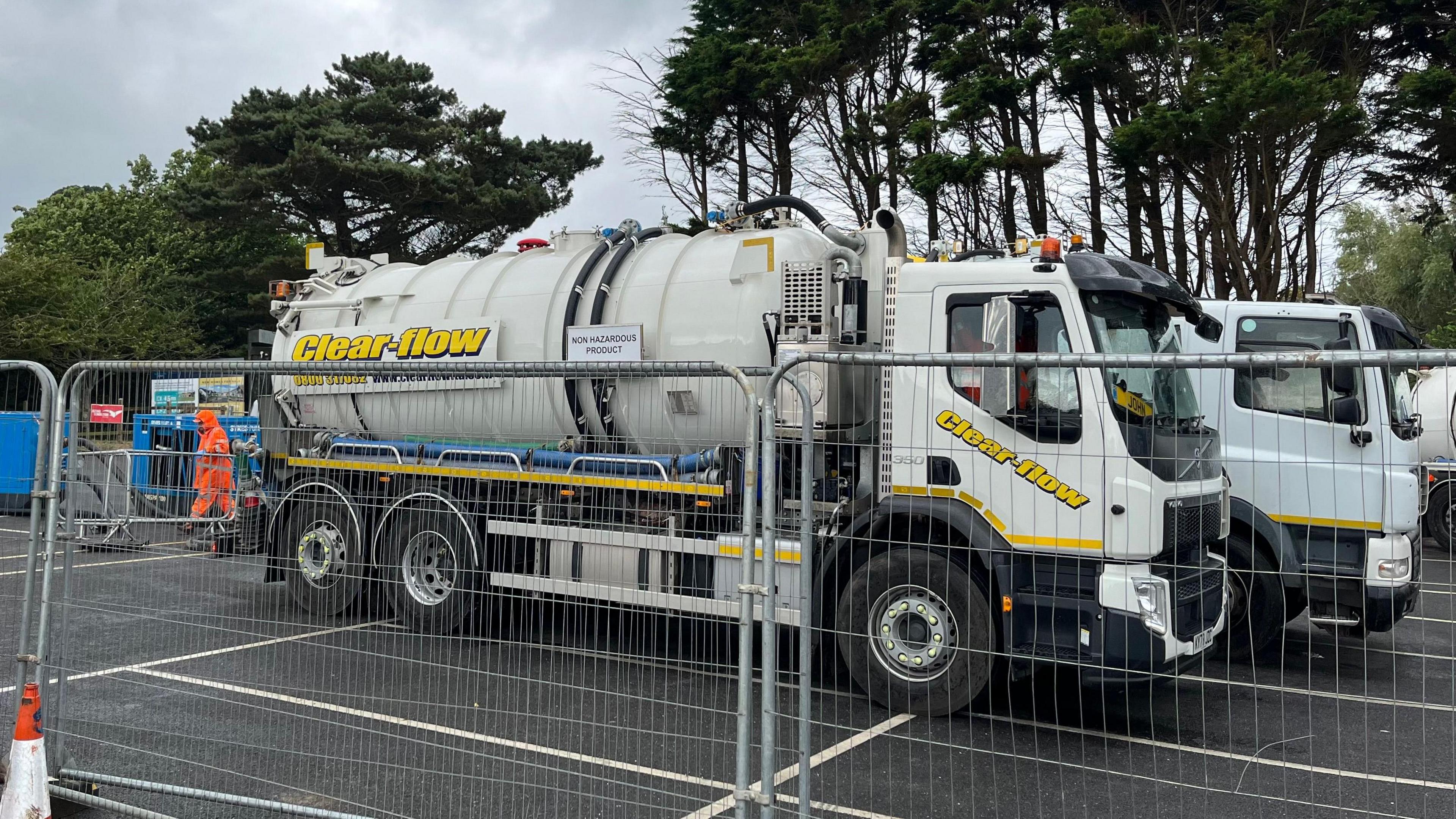 A white tanker with Clear Flow written on it in yellow letters behind a metal fence.