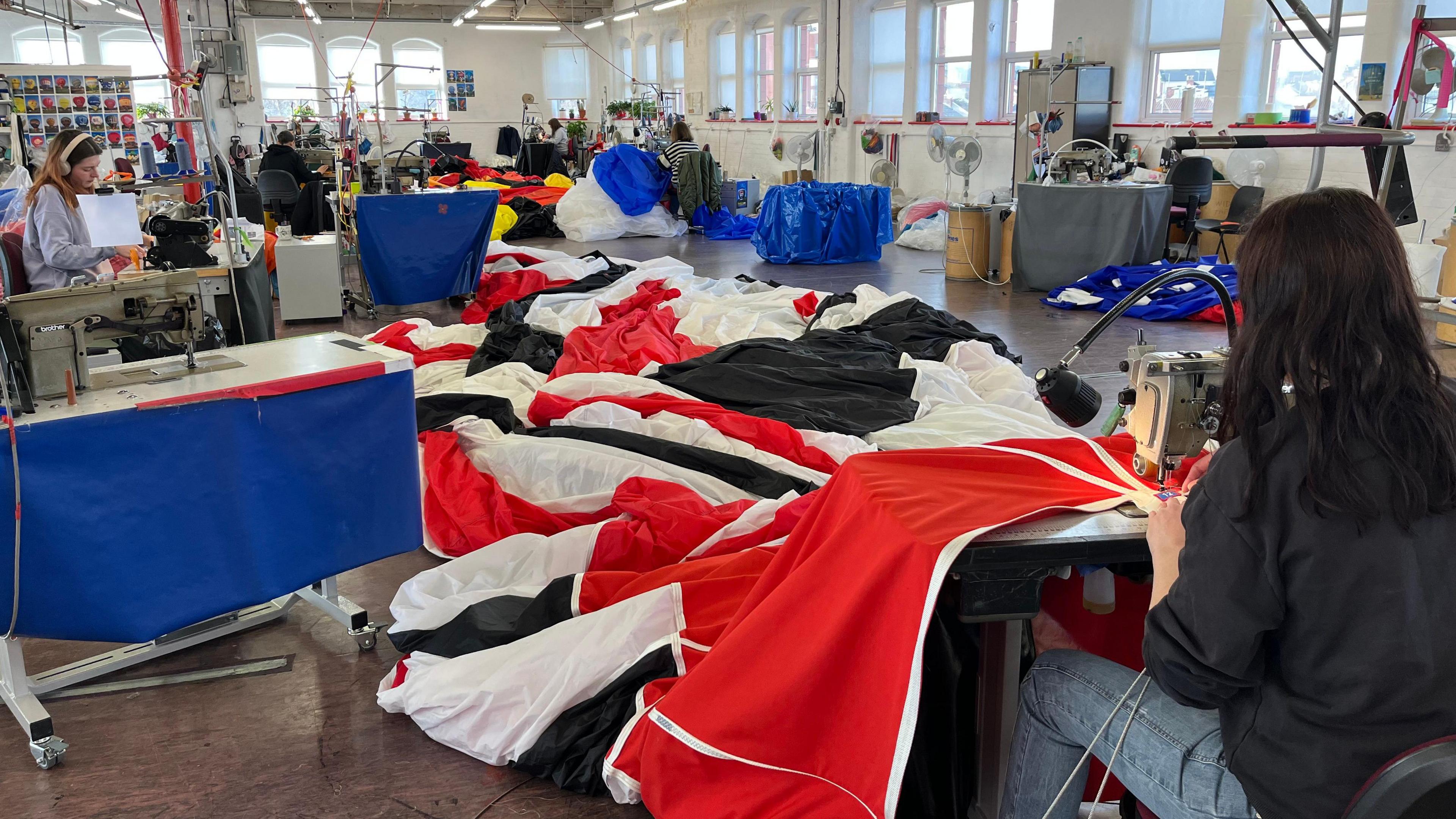 A woman sitting at a sewing machine working on the material for a hot air balloon. The fabric is red, black and white.