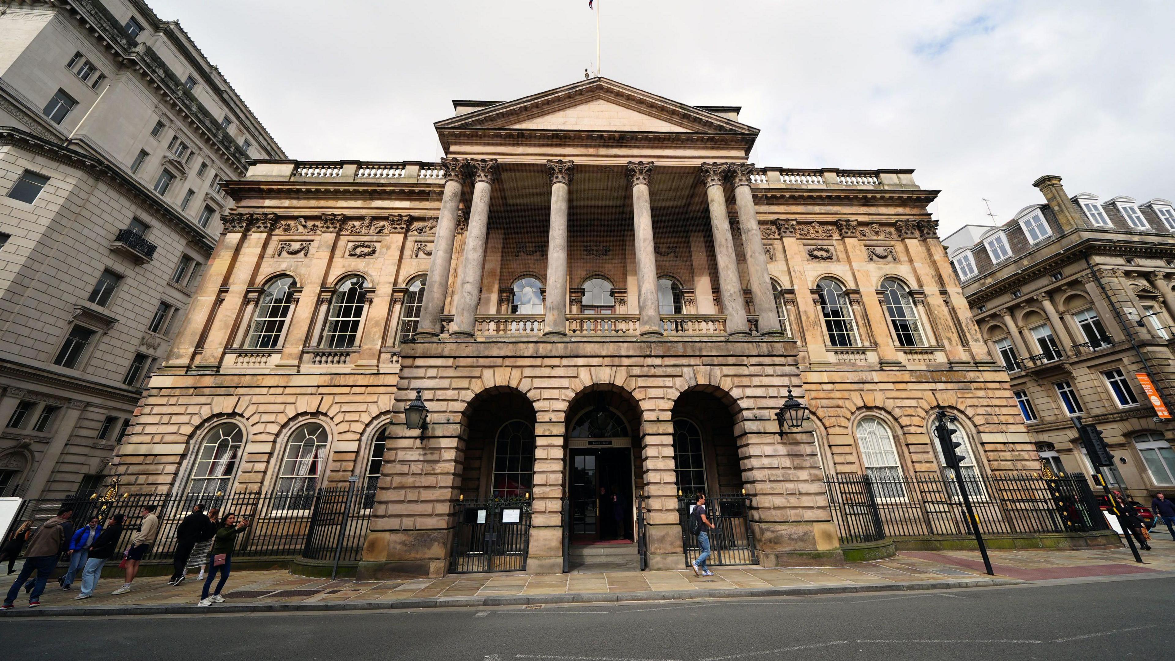 Street-level photograph of the front of Liverpool Town Hall. A few pedestrians are walking along the pavement.