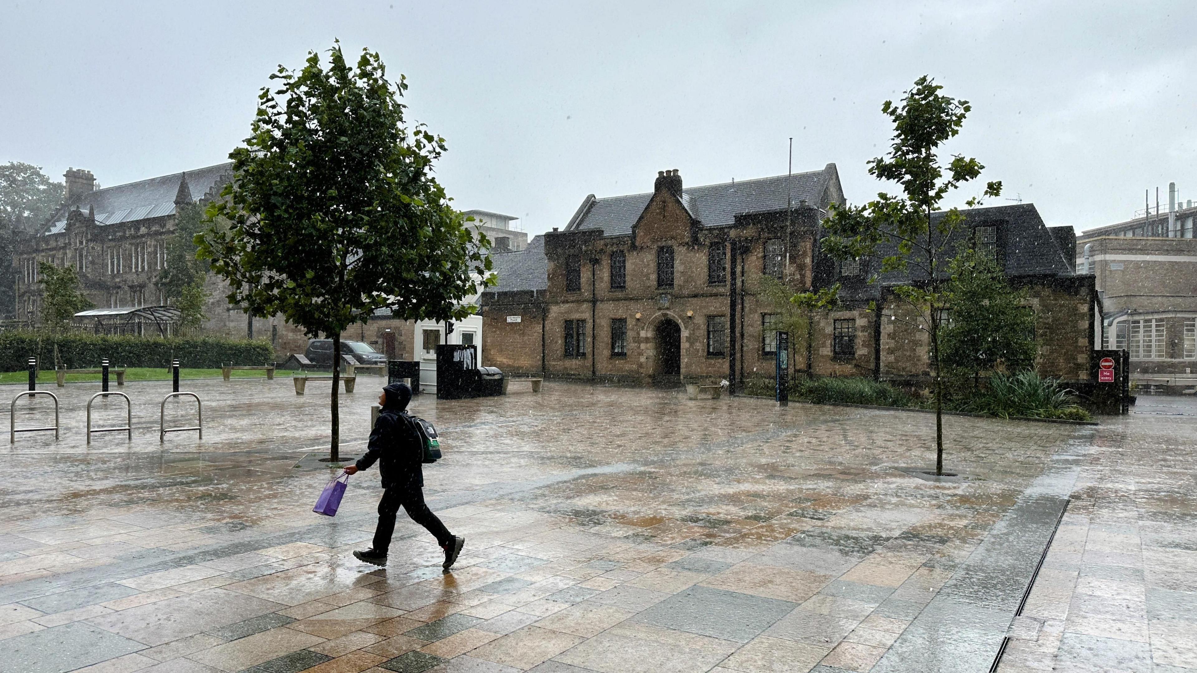 Person walks next to building in Glasgow with heavy rain causing surface flooding