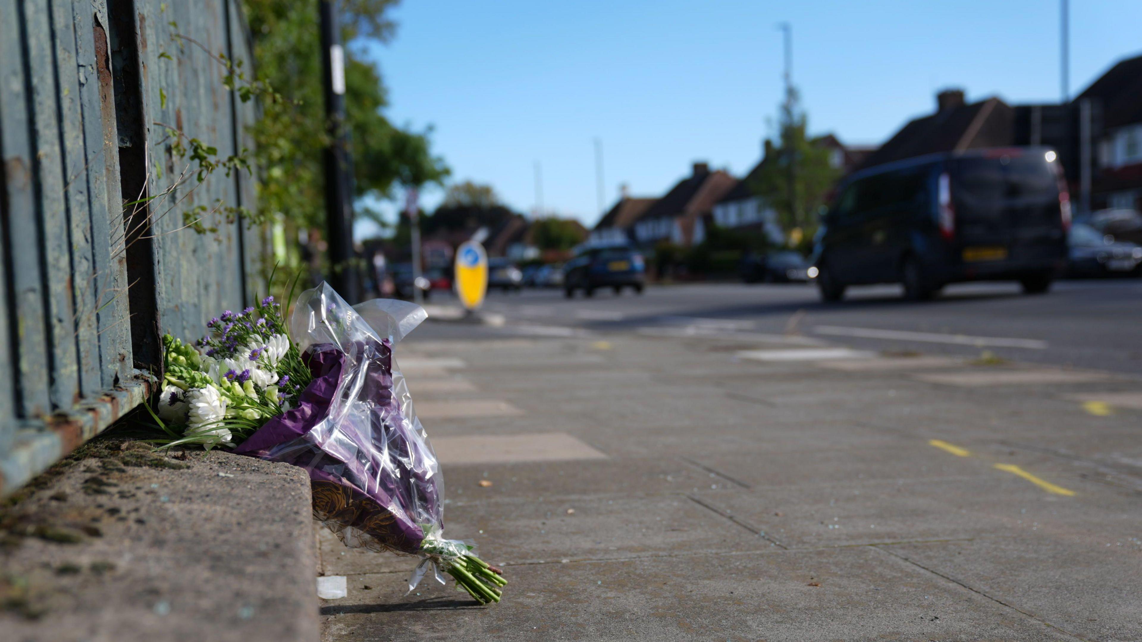 A single bouquet of flowers sitting against a fence on a path next to where the crash happened.