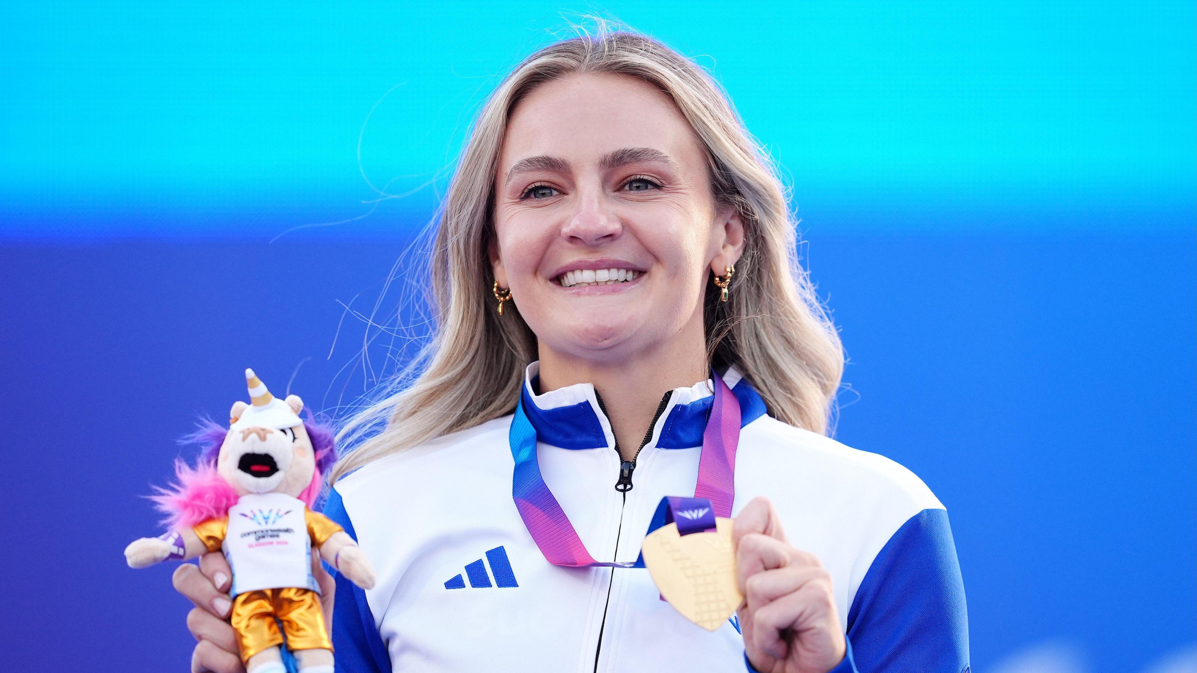 Melanie Woods holding a tiny version of the unicorn mascot of the games, as well as the gold medal round her neck