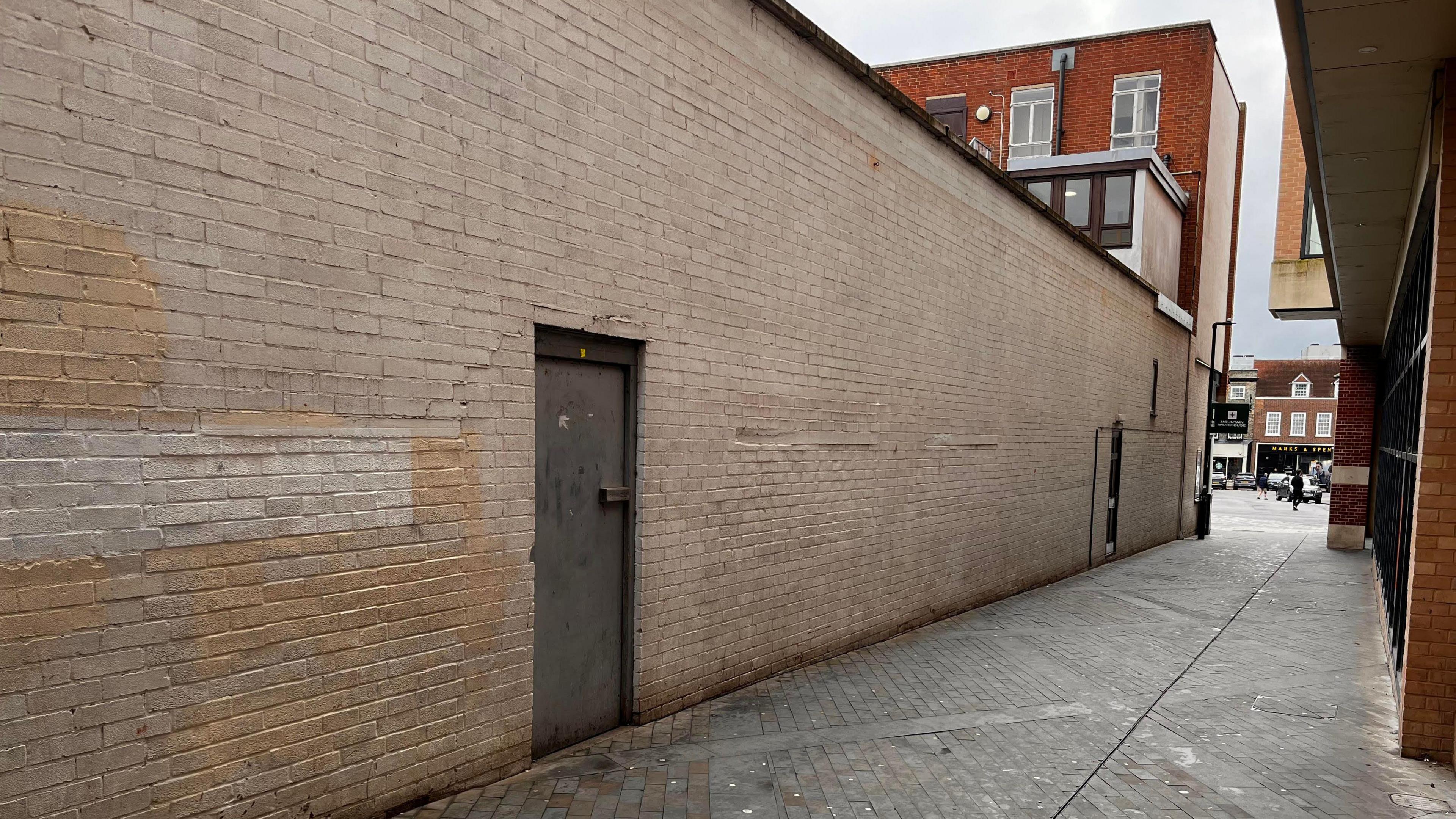 A cream wall alongside an alleyway, there is a door in the wall.