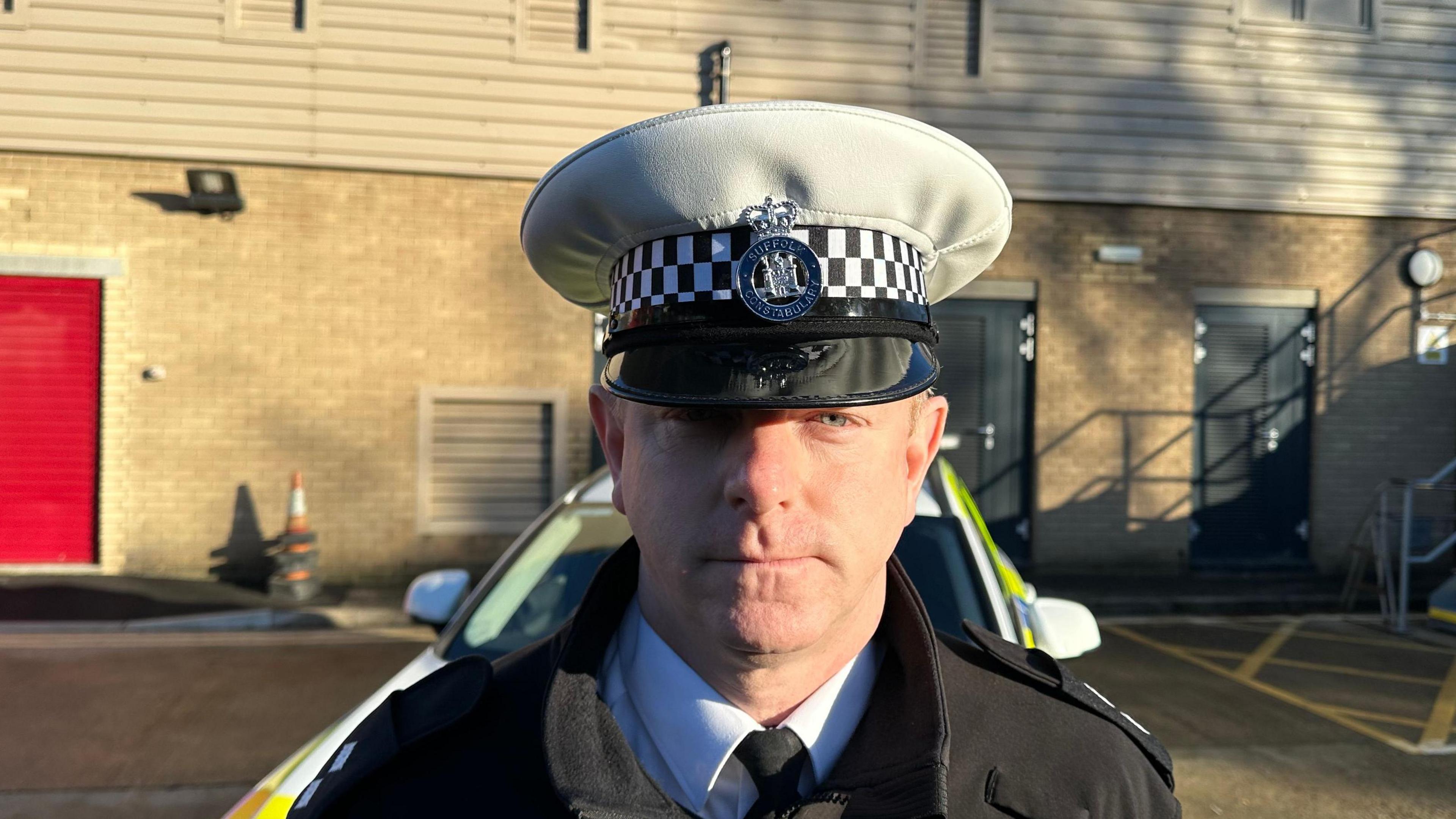 Acting inspector Andy Smith wearing a police hat stood in front of a police car