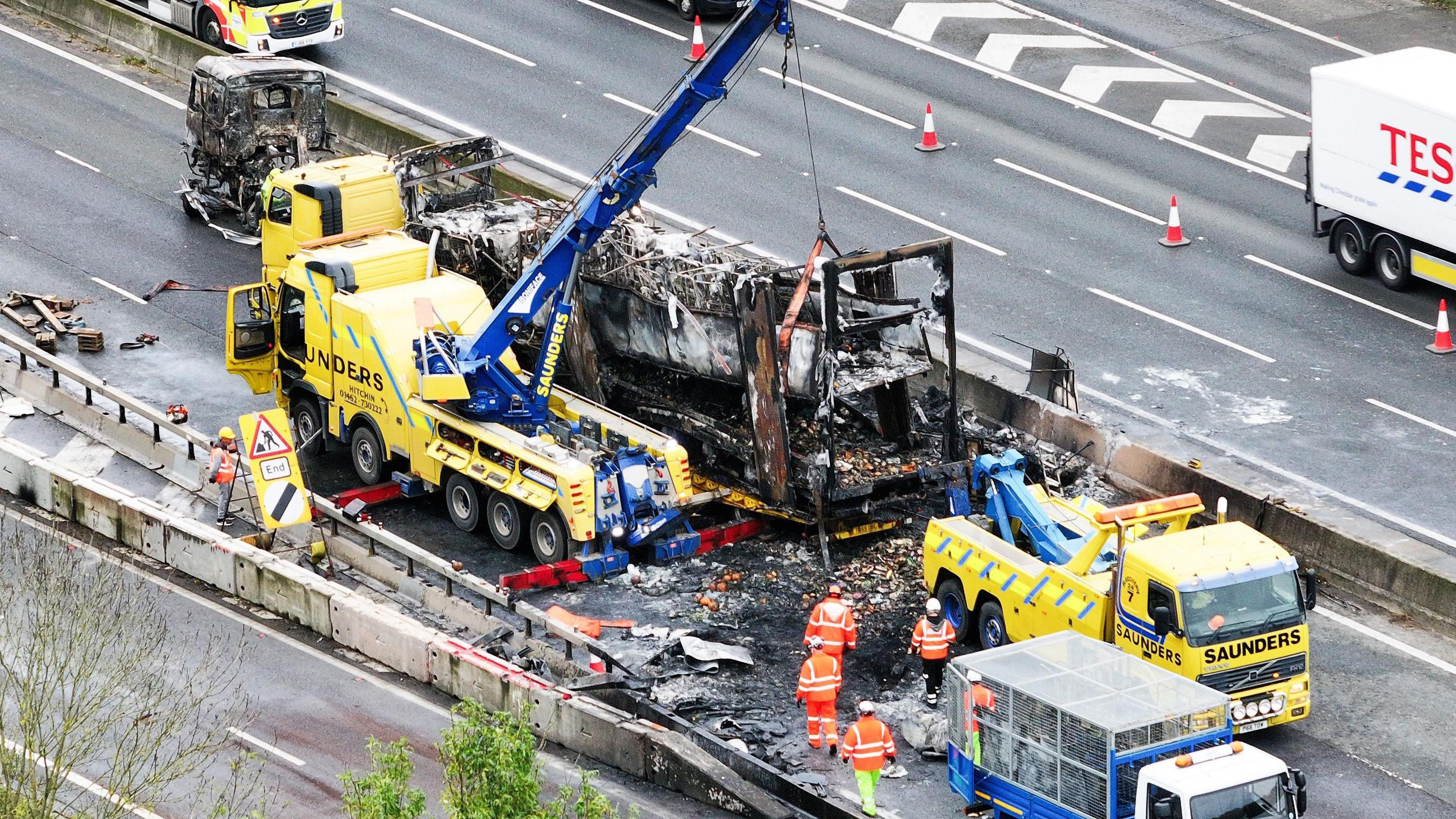 An aerial shot of a burnt out vehicle on a section of motorway. Fire hoses are visible.