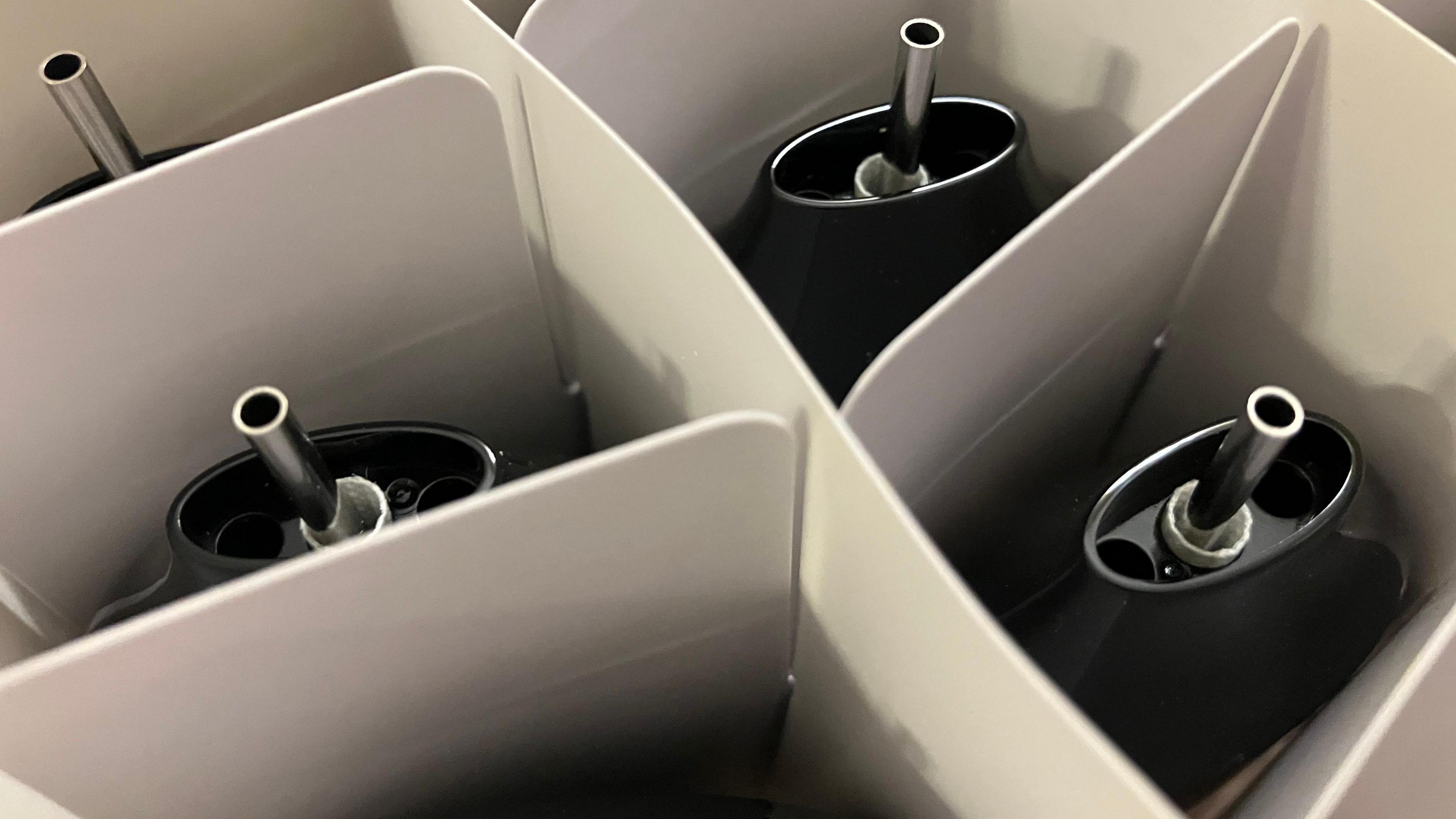 An aerial close-up image of three black disposable vapes, that have been put in a box. They are separated by white cardboard packaging.