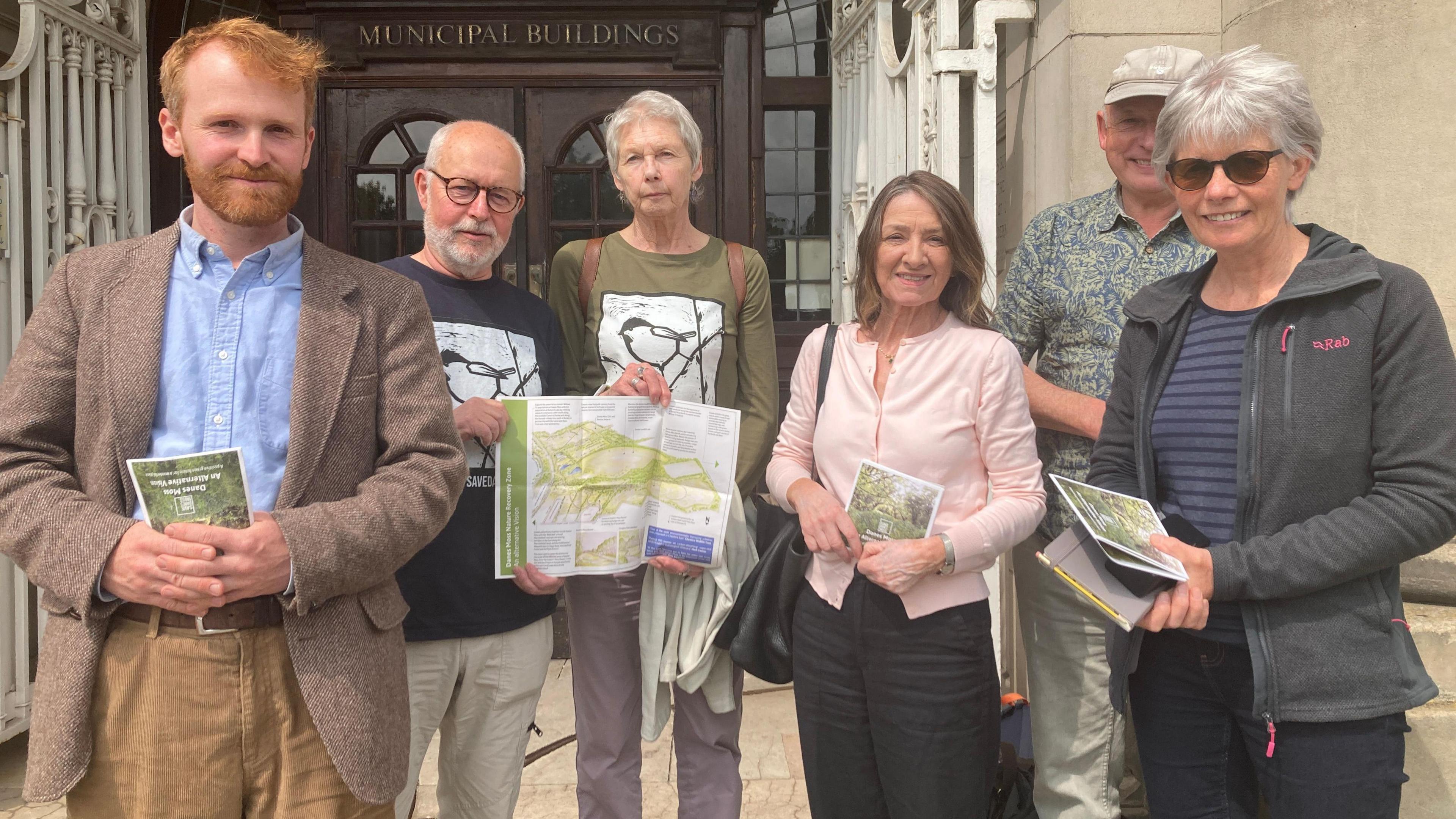 Campaigners from the Danes Moss Trust stand outside a council building holding up leaflets expressing their objection to the proposals.