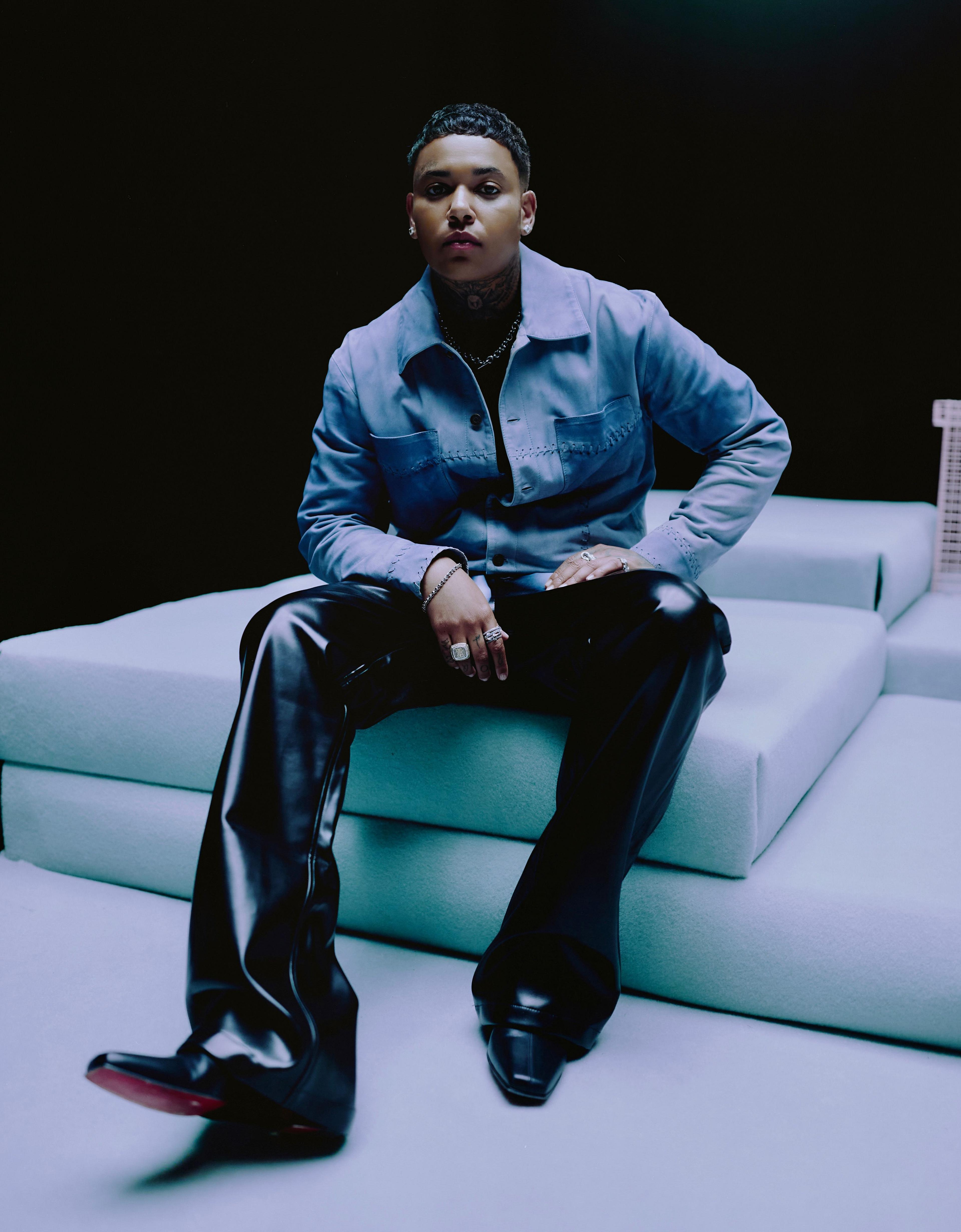 Promotional photo of KWN, sitting down in a denim shirt and black leather trousers
