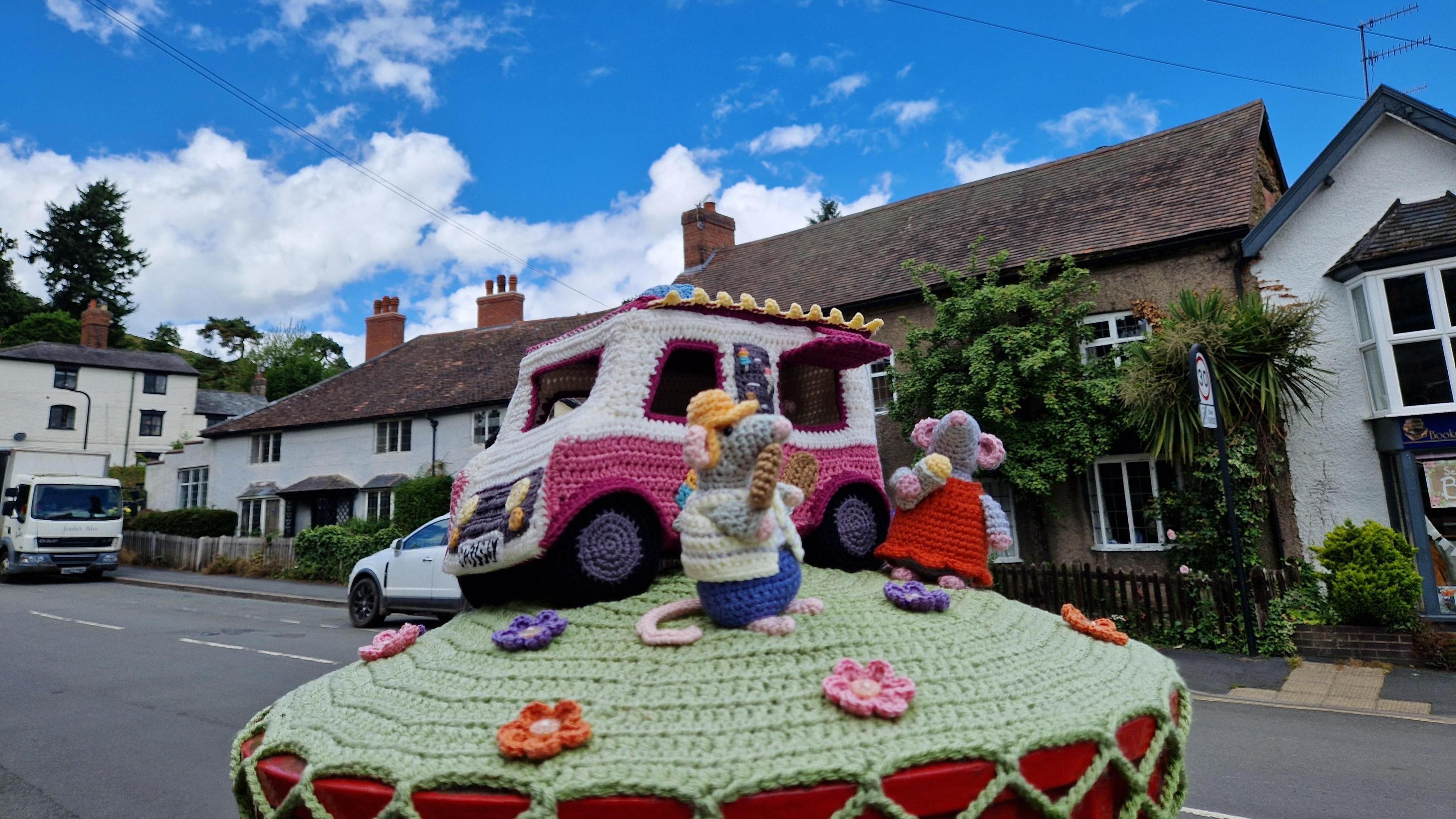 A knitted scene showing woolly figures on top of a post box in Church Stretton