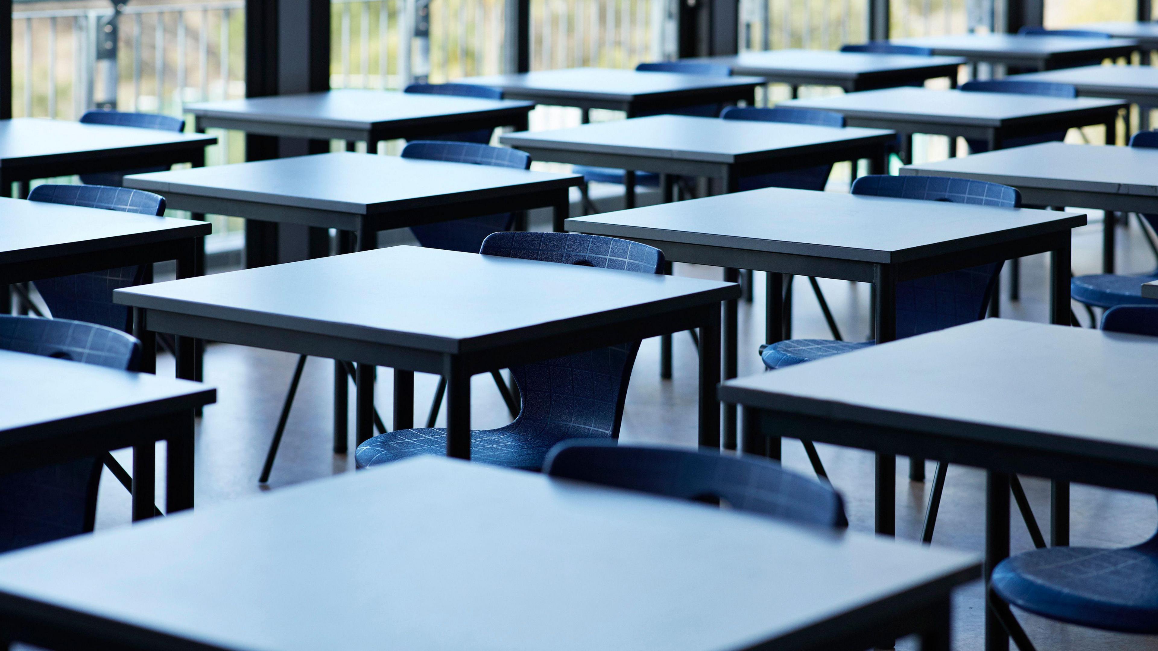 Rows of empty chairs and tables in a school classroom.