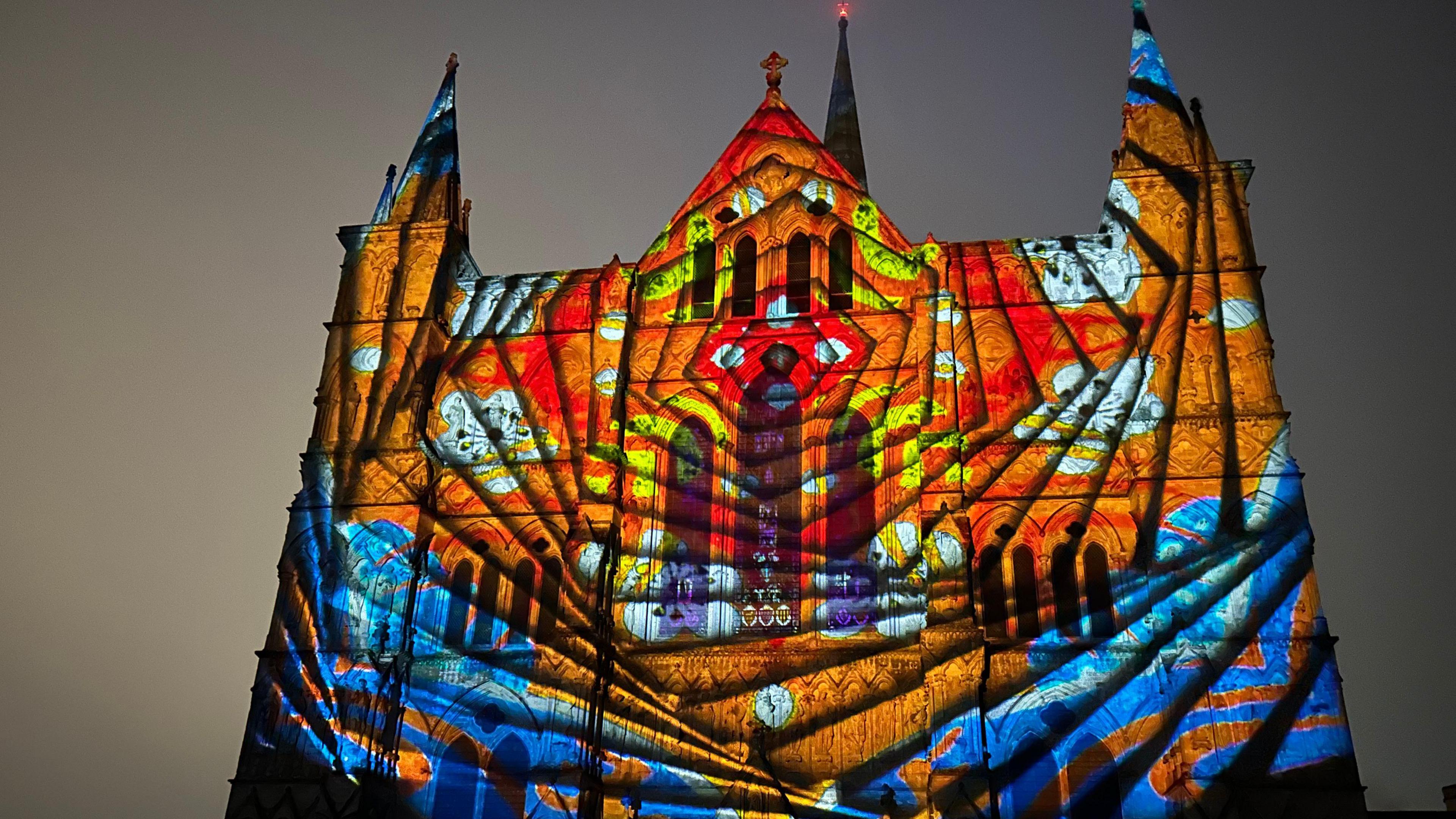 The front of Salisbury Cathedral in the dark, but with a huge coloured lights display projected onto it.