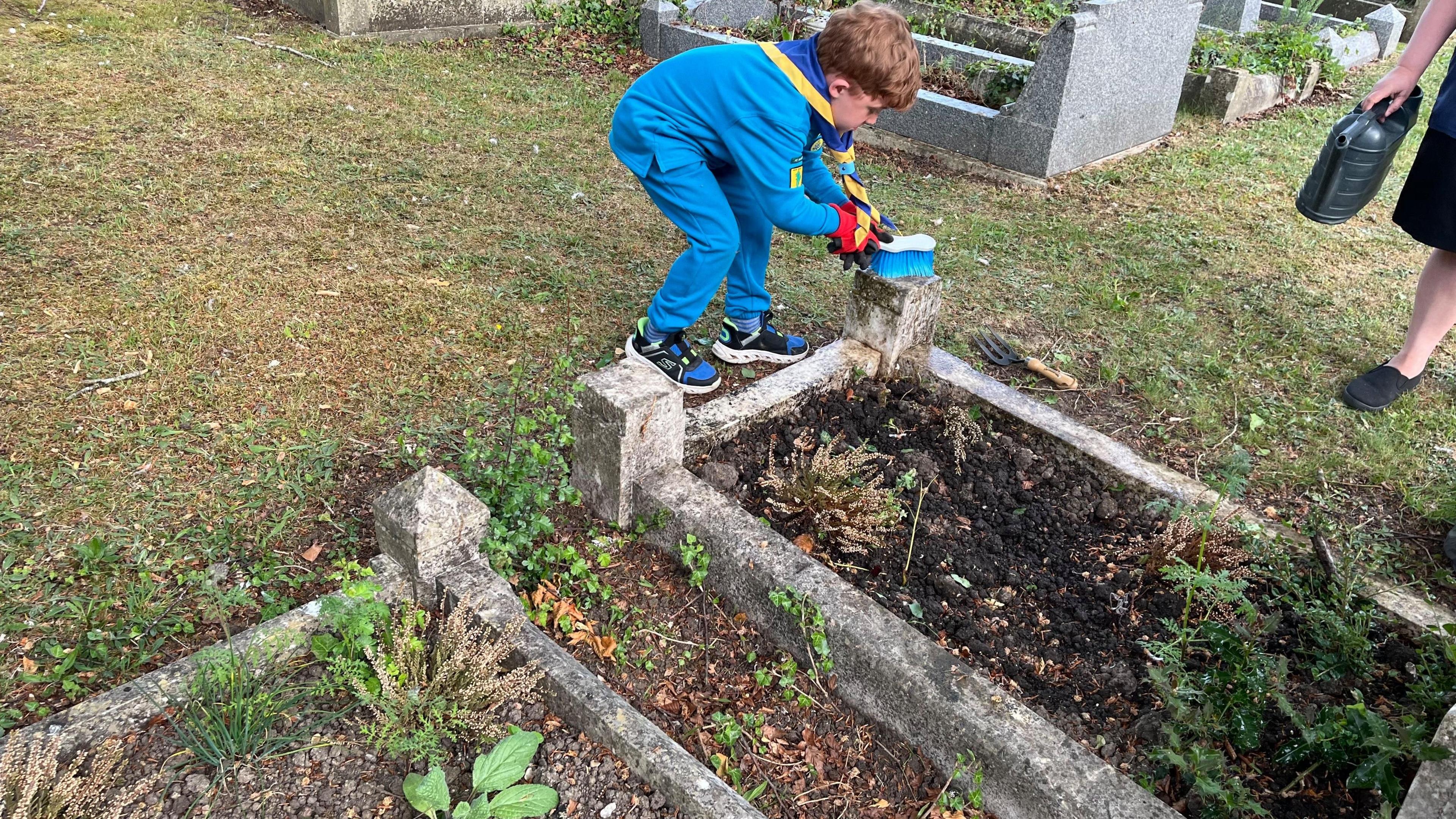 A young boy in all blue scrubbing concrete corners of a grave