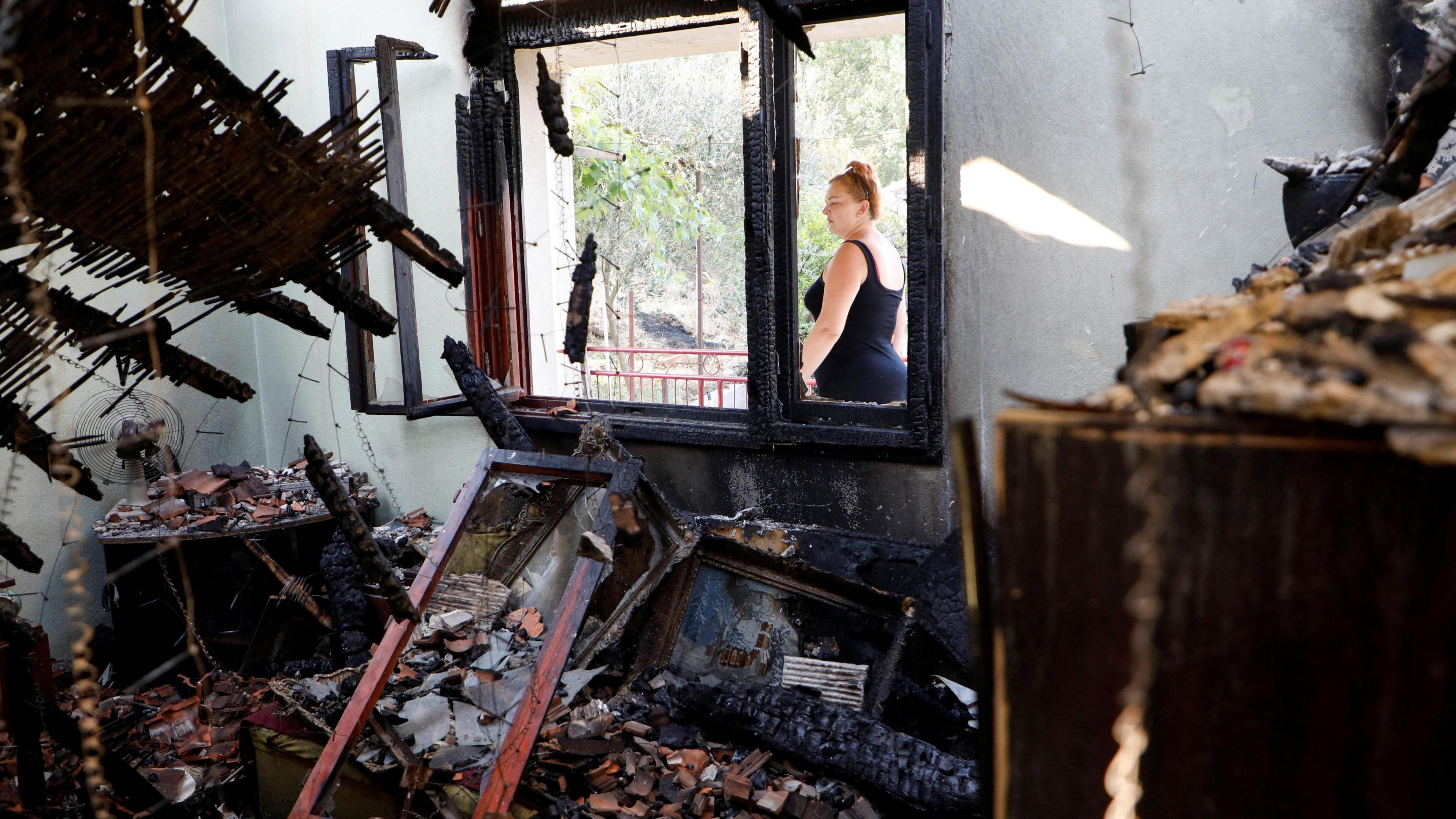 A woman in a black sleevless dress looks passes by the burnt out shell of her home in Piperi Village, Montenegro.