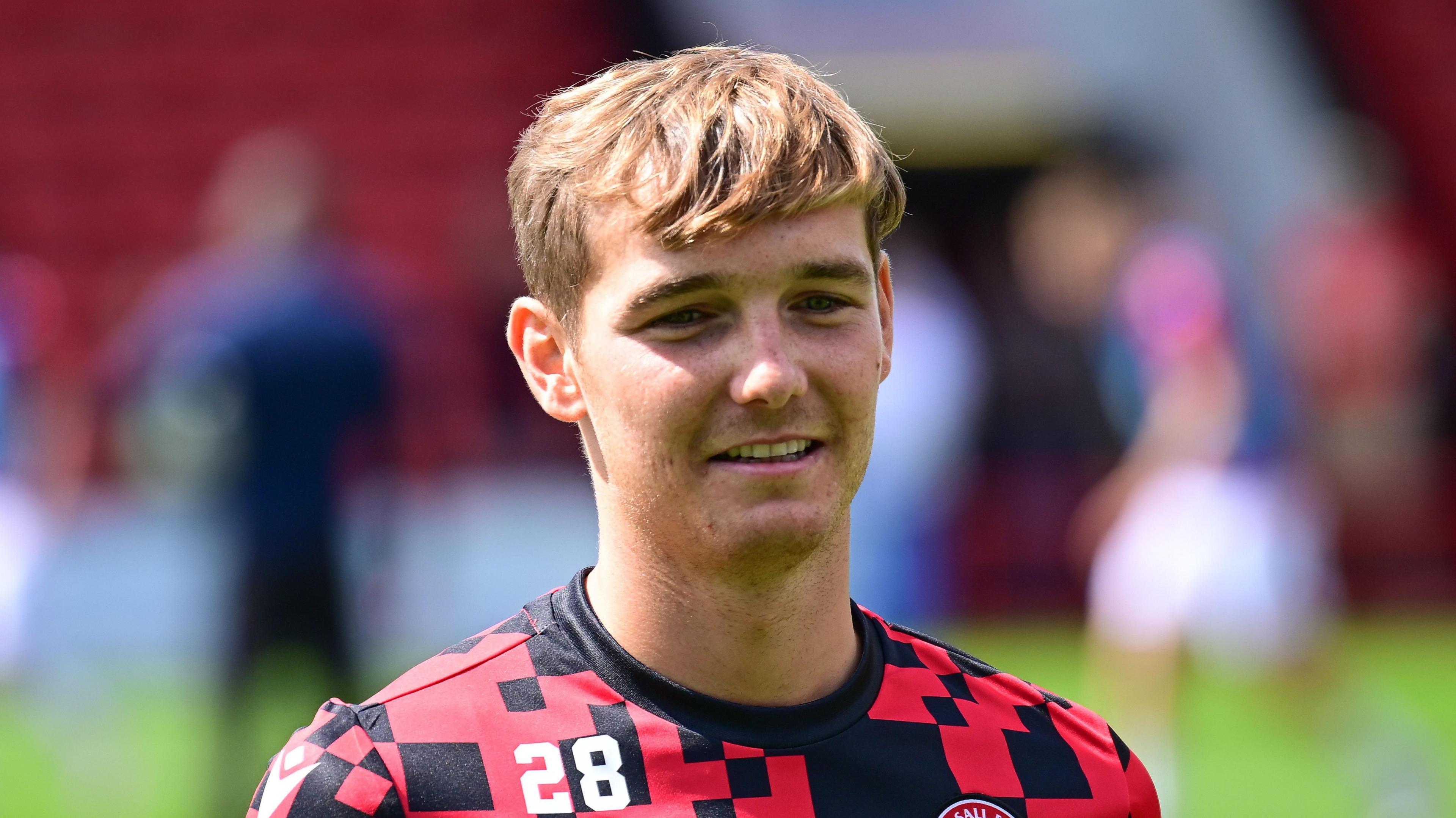 Lewis Warrington with number 28 on the right side of his chest and the Walsall badge on the left, in a red and black T-shirt training top