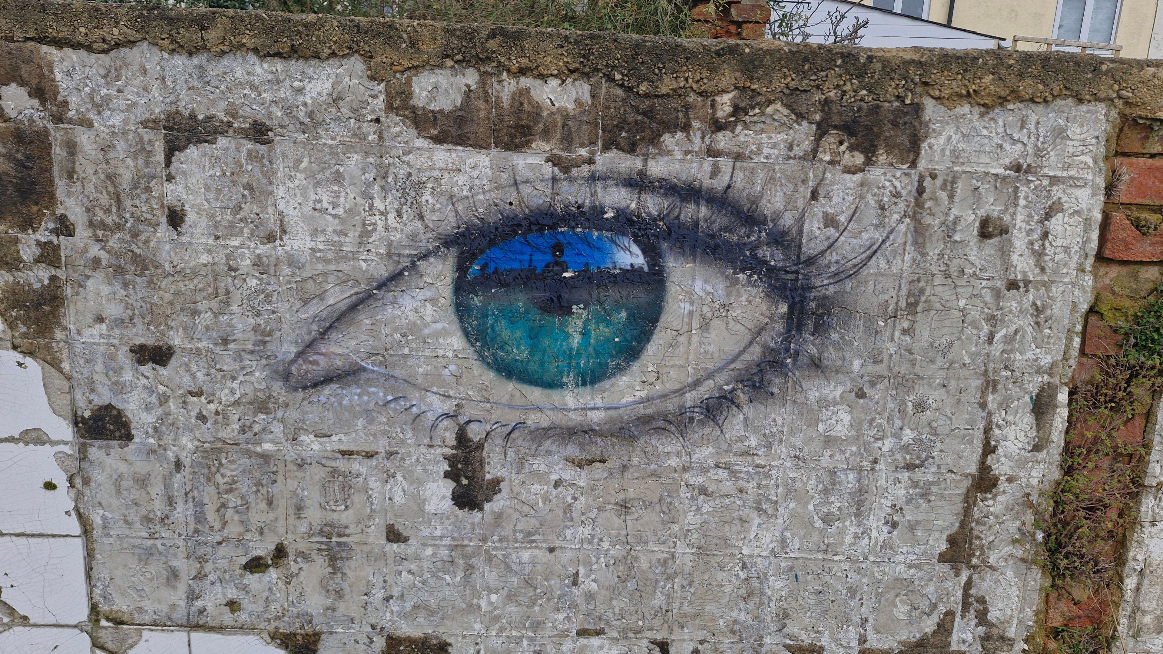 A large blue eye painted on a grey wall with extended eye-lashes