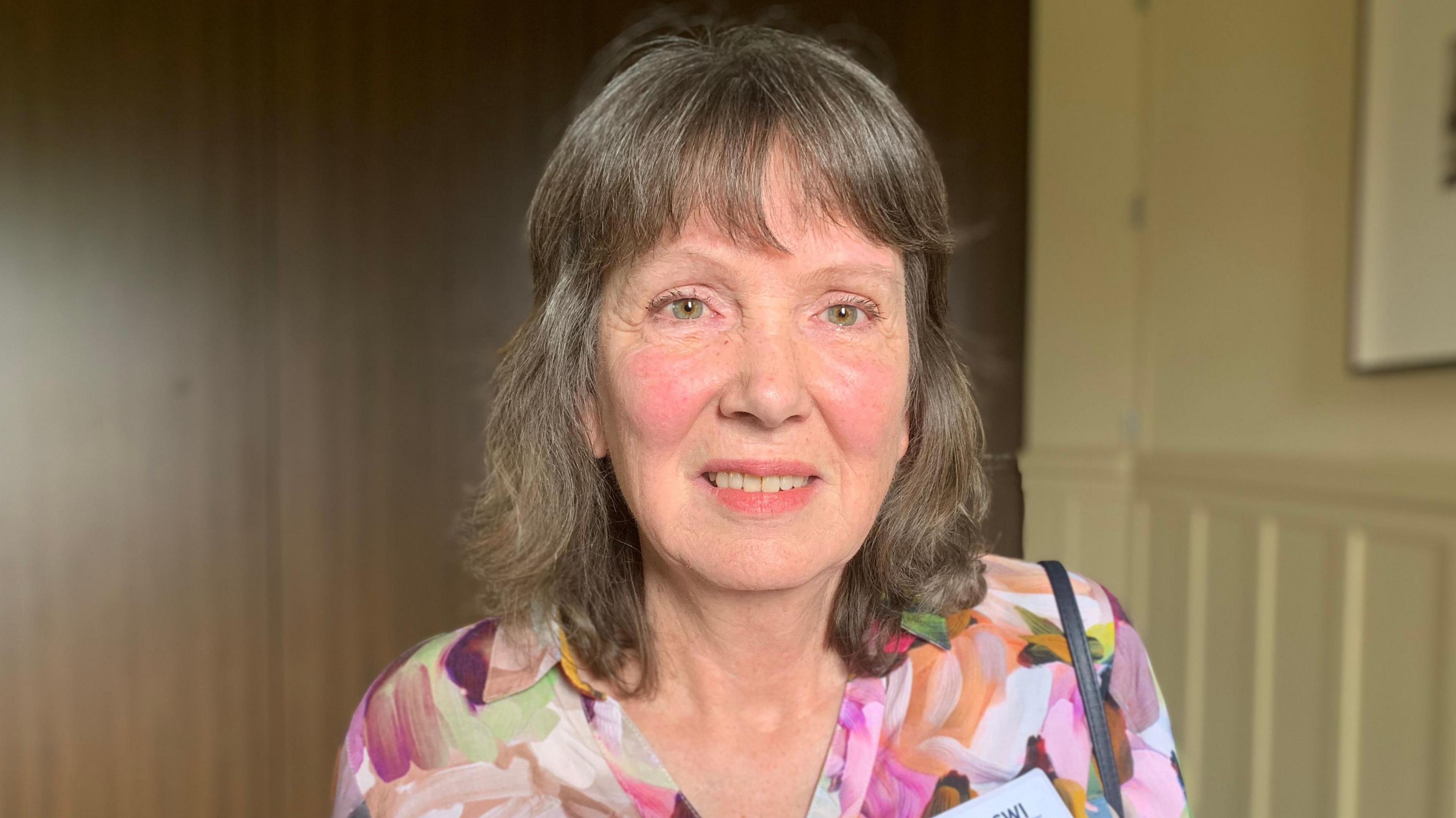 A woman with brown hair in a colourful floral blouse