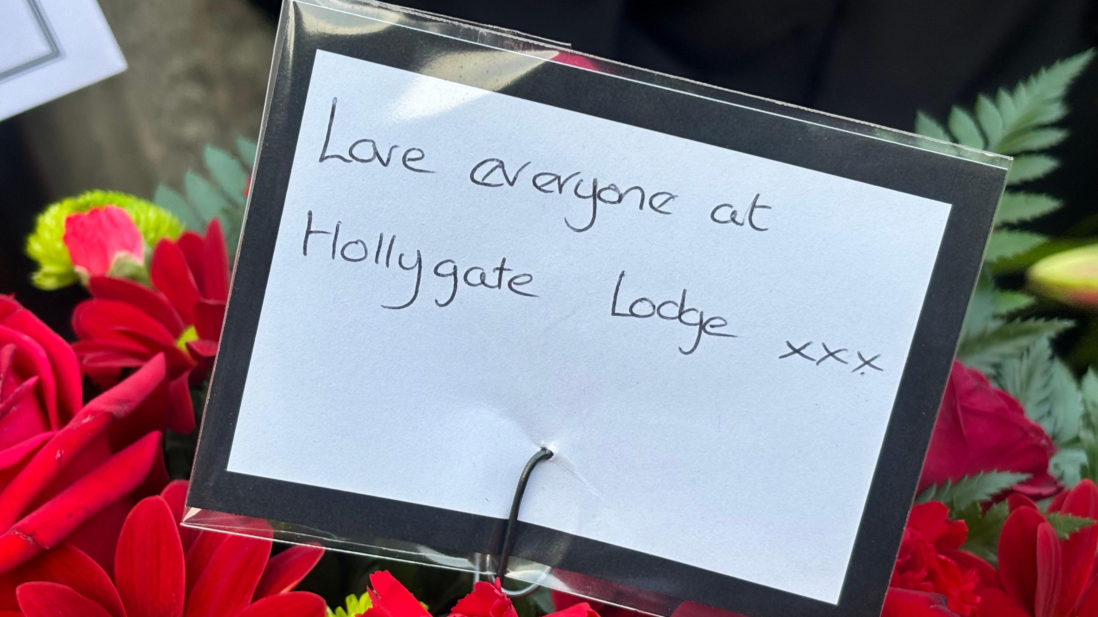 A note on red funeral flowers reads "Love everyone at Hollygate Lodge xxx"
