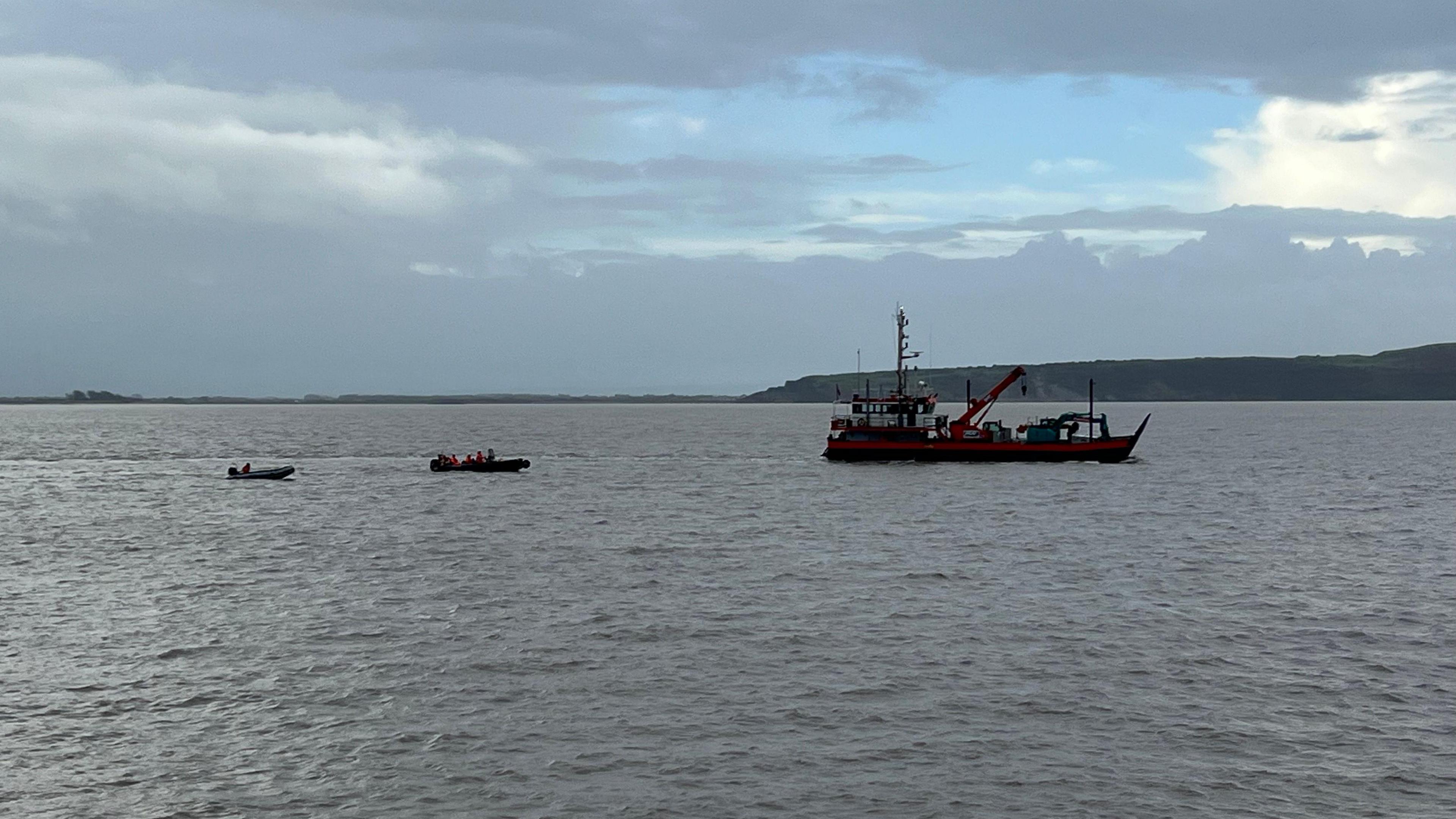 Boat in sea with tugboat with views of the Severn Estuary. there's blue sky at the top of the image and a lot of brown sea at the bottom of the image.