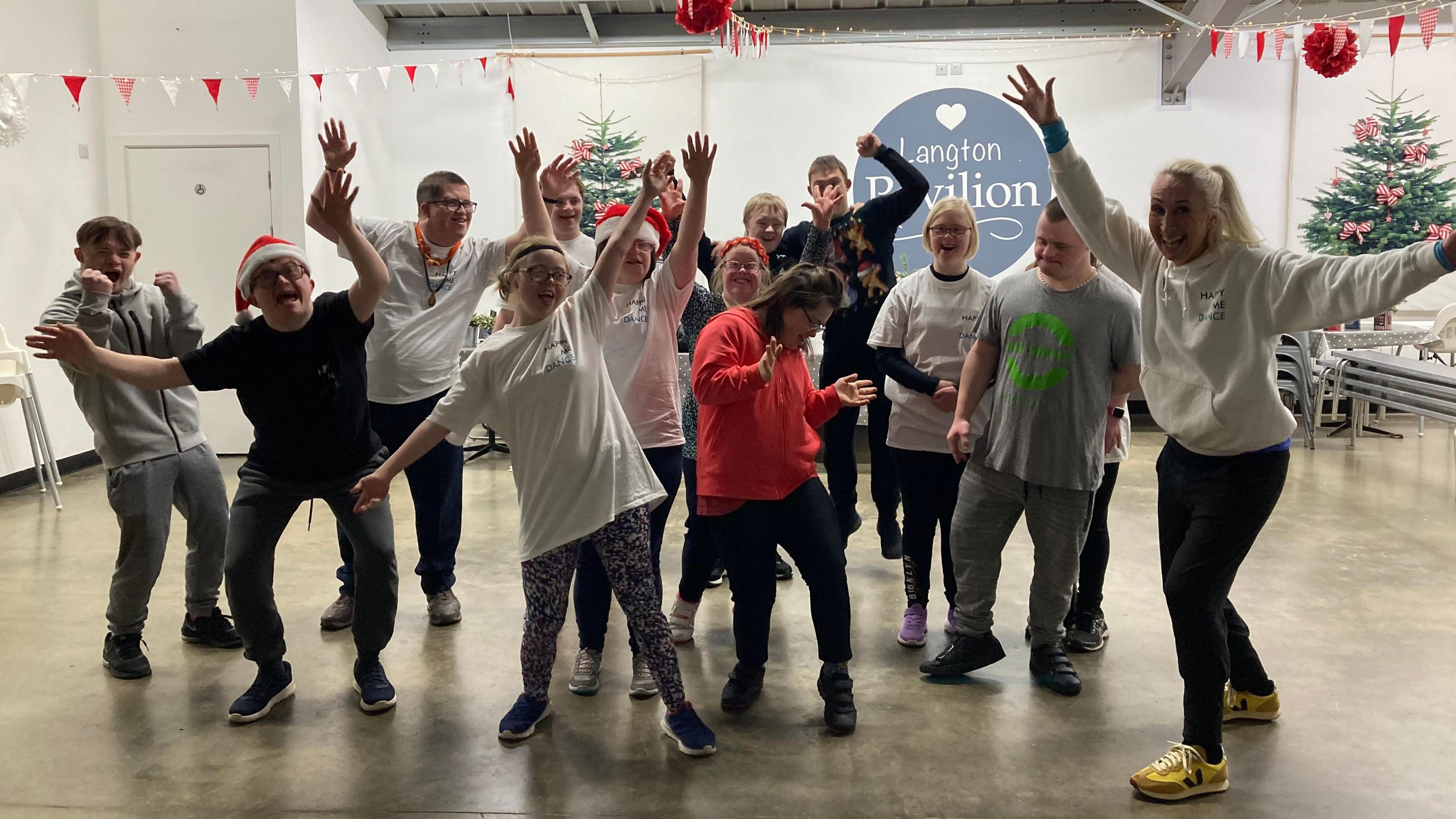 A group of 14 people, most with their hands in the air. They are all looking at the camera. 