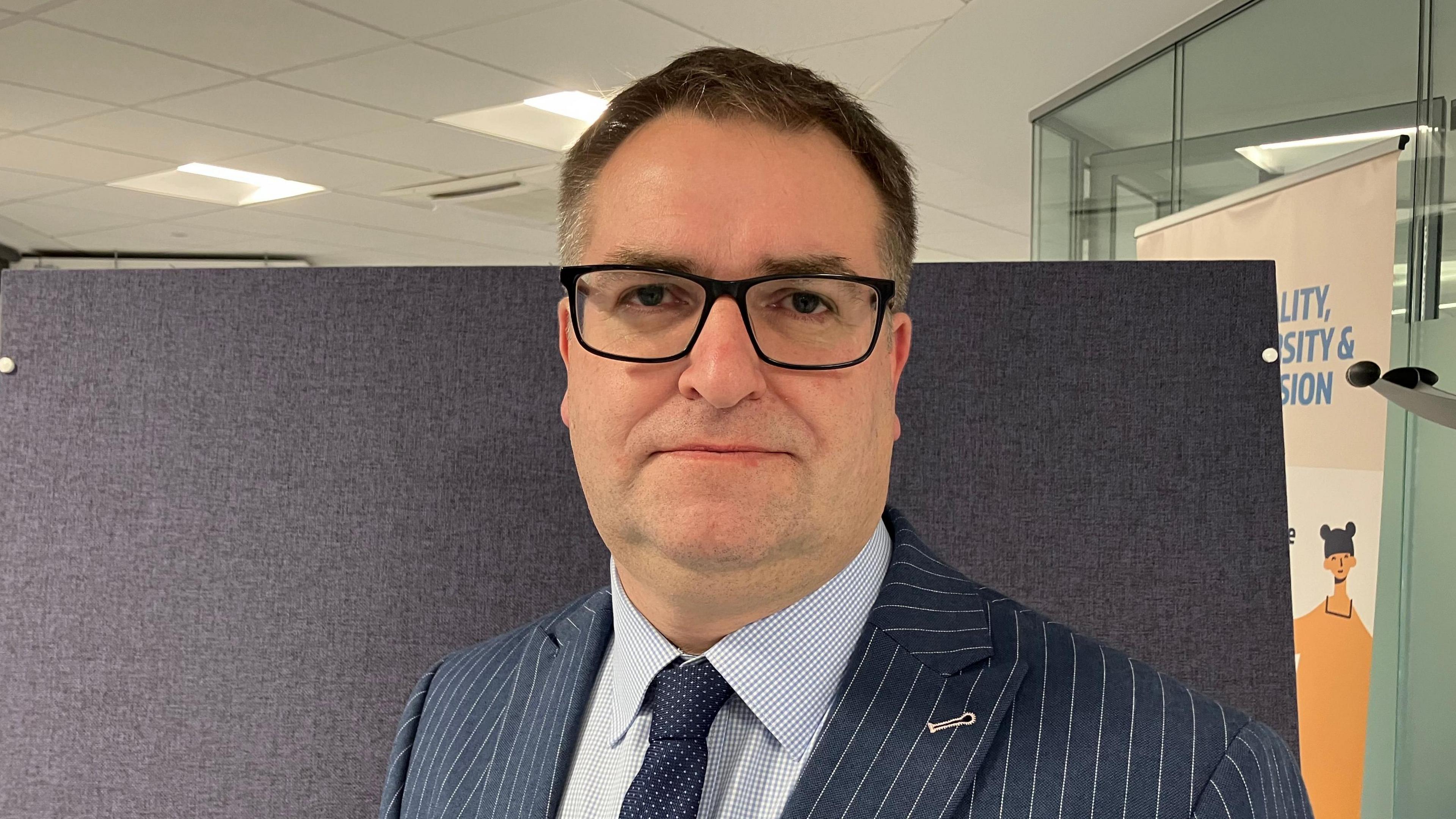 A head and shoulders picture of Richard Walker, Head of Parking for the North Essex Parking Partnership. He is wearing a pinstripe suit and black-framed glasses.