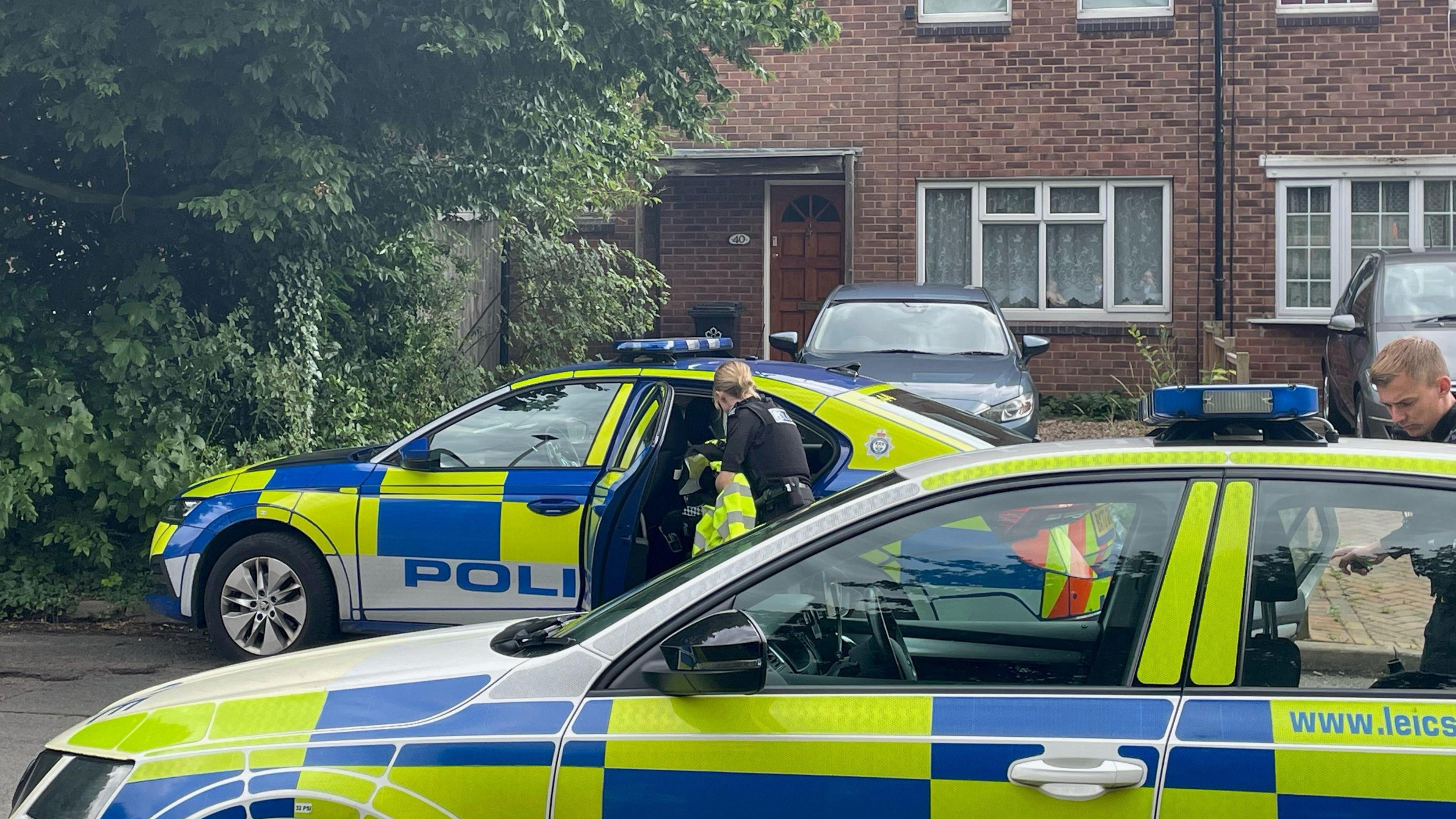 Police officers and two police cars outside a house in Hopyard Close in Leicester