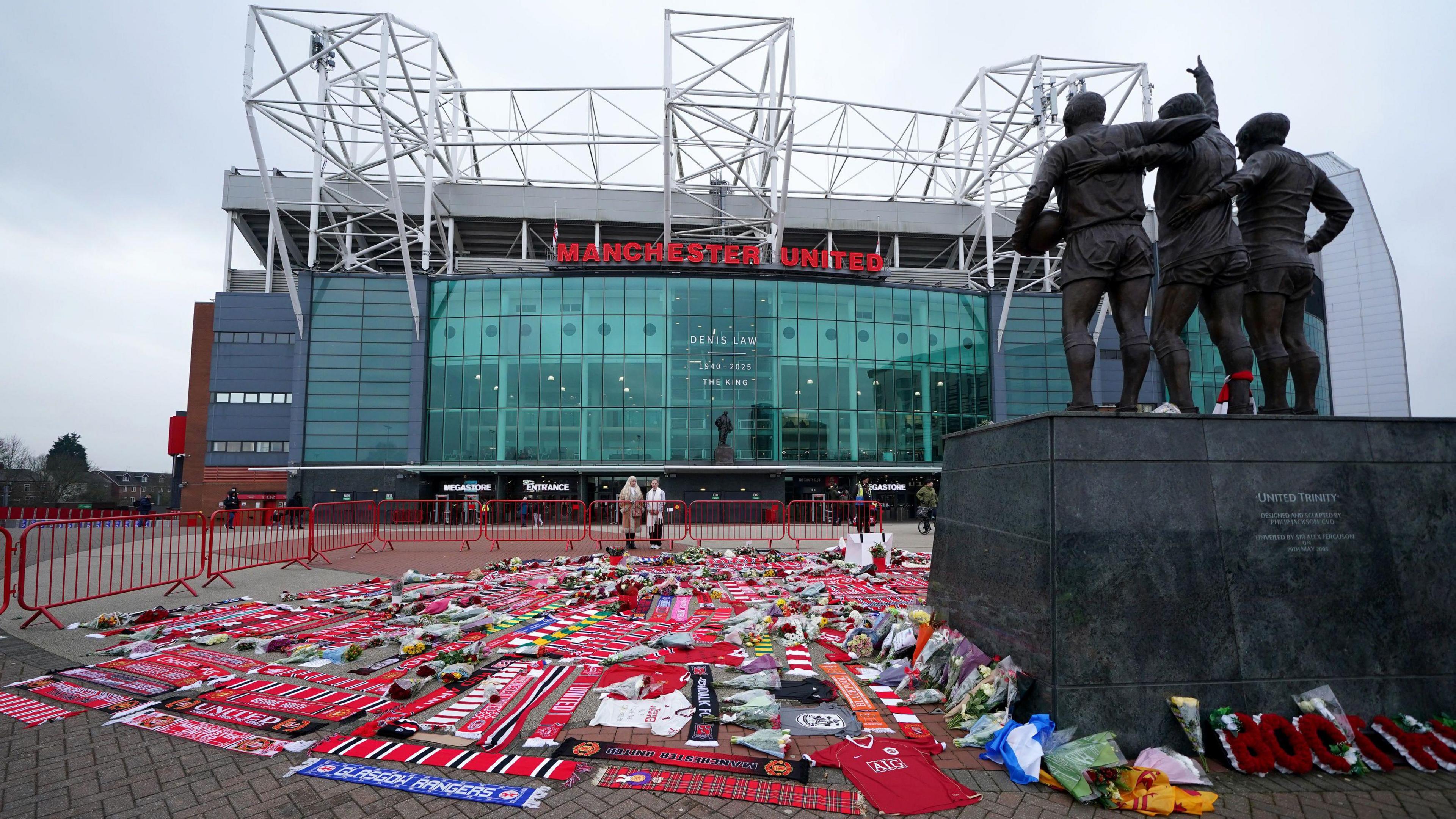 Floral tributes and football scarves laid at the foot of the Trinity statue atOld Trafford.