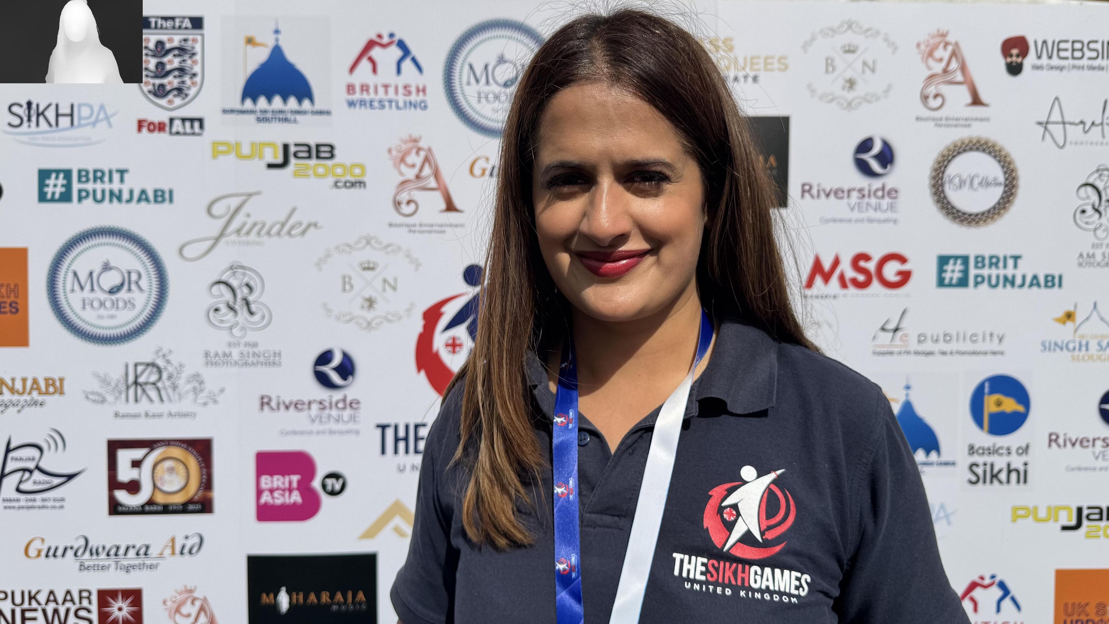 Mandeep wears a navy polo shirt with the Sikh games logo. She is smiling and has shoulder length brown hair.