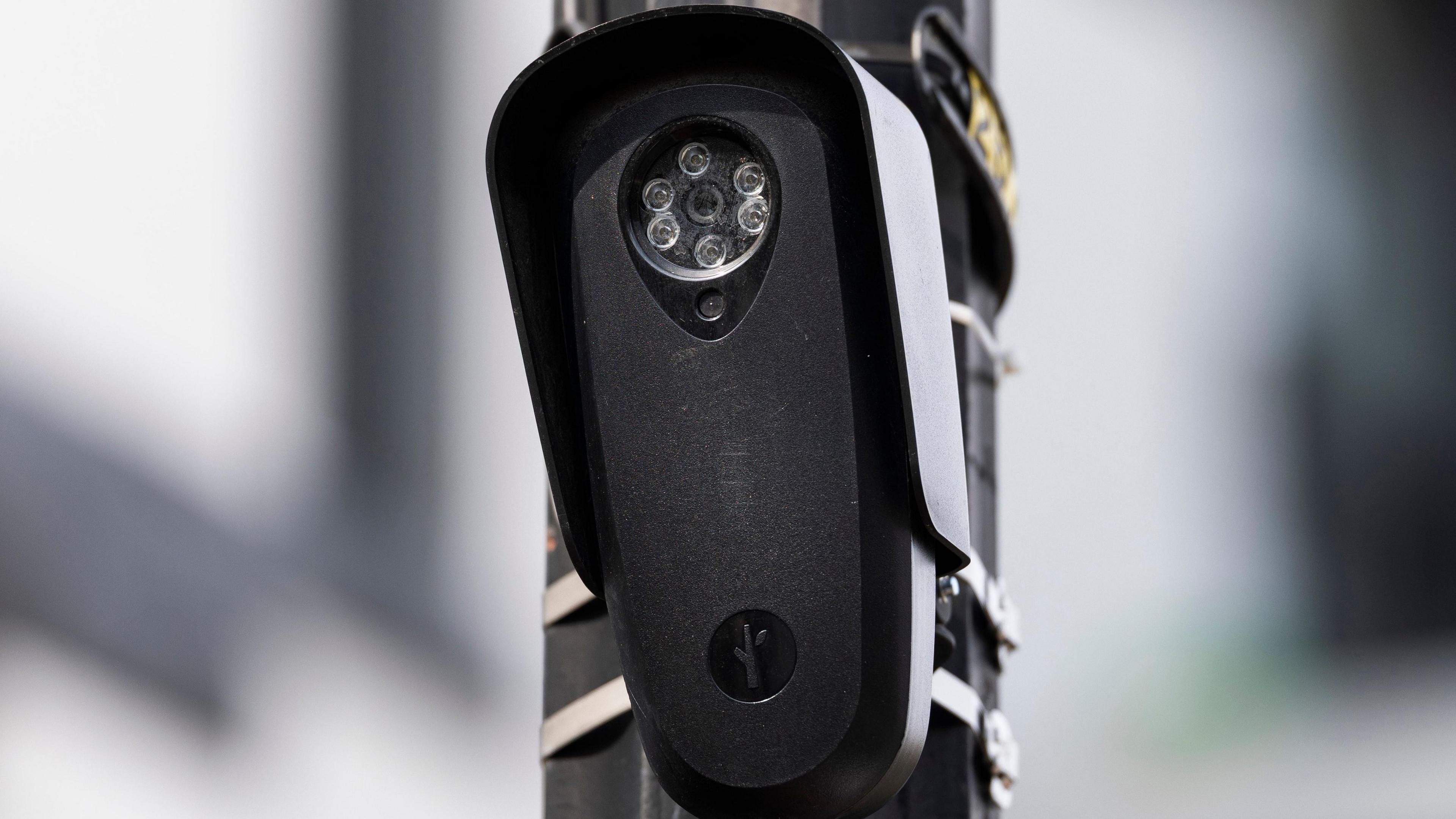 An unobtrusive and black Flock camera attached to a pole near an intersection in Washington DC.