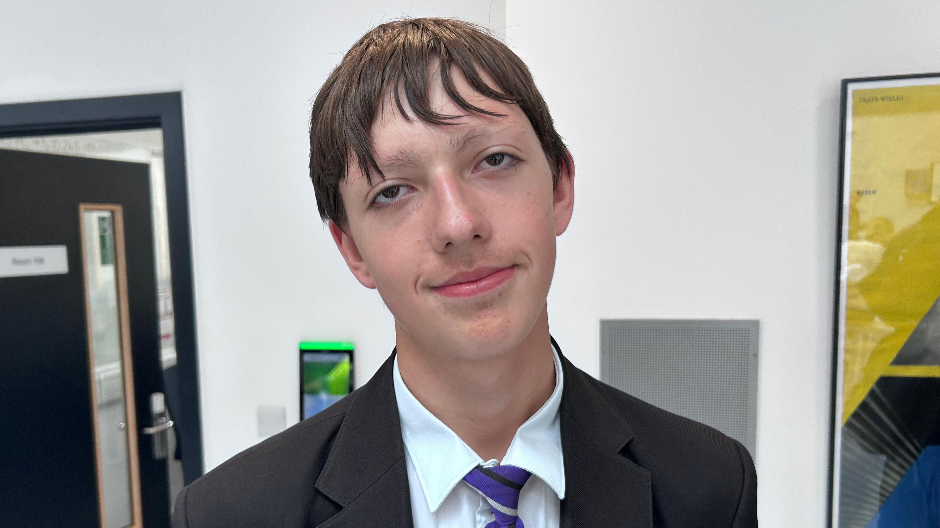 A boy in a school uniform with a purple, white and black coloured tie.