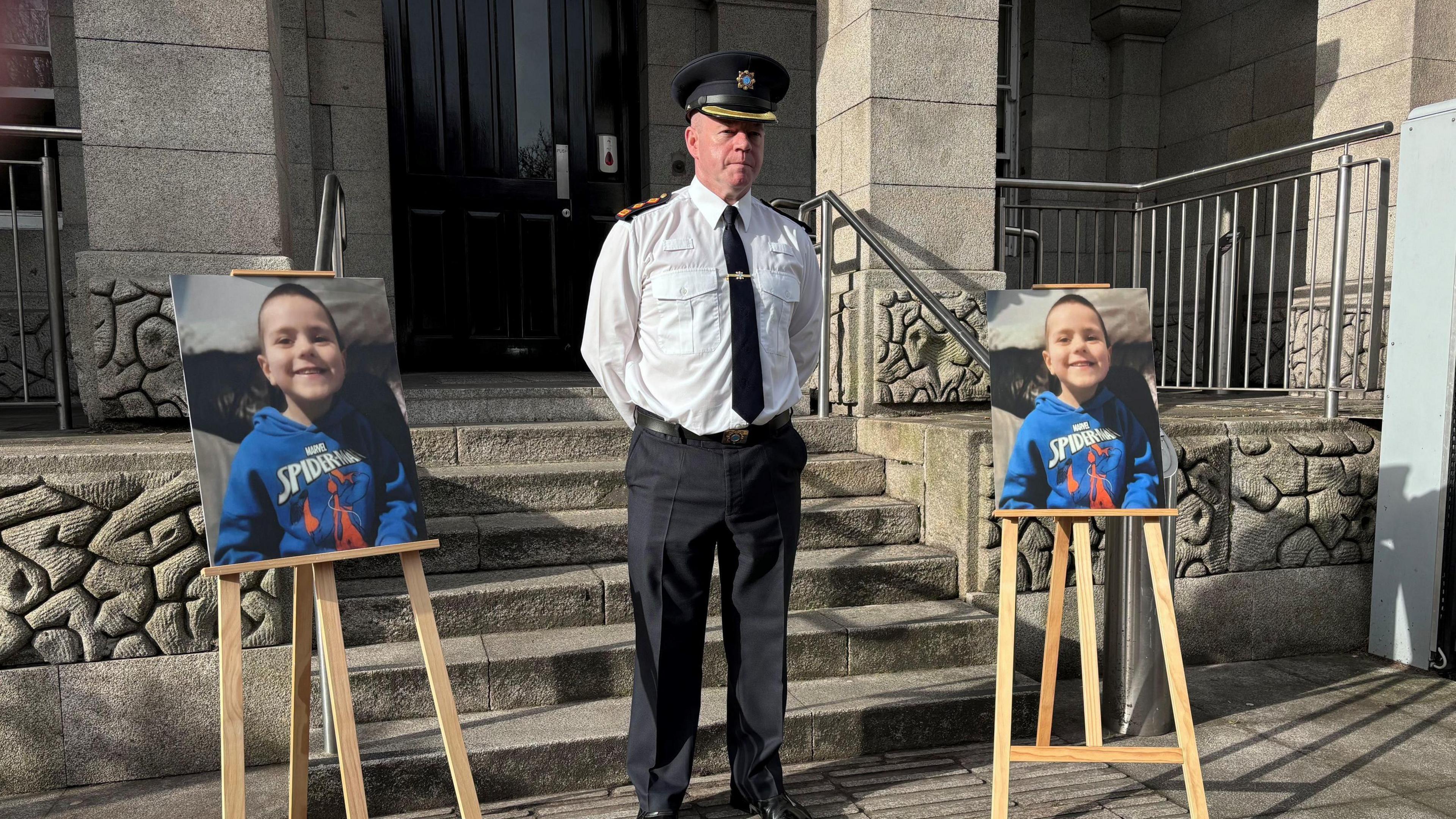 Ch Supt Alan McGovern, dressed in garda uniform, pictured during a press conference outside Dundalk Garda station.  He is flanked by two large photos of Kyran Durnin, propped up on wooden stands, in front of the steps of the station. 