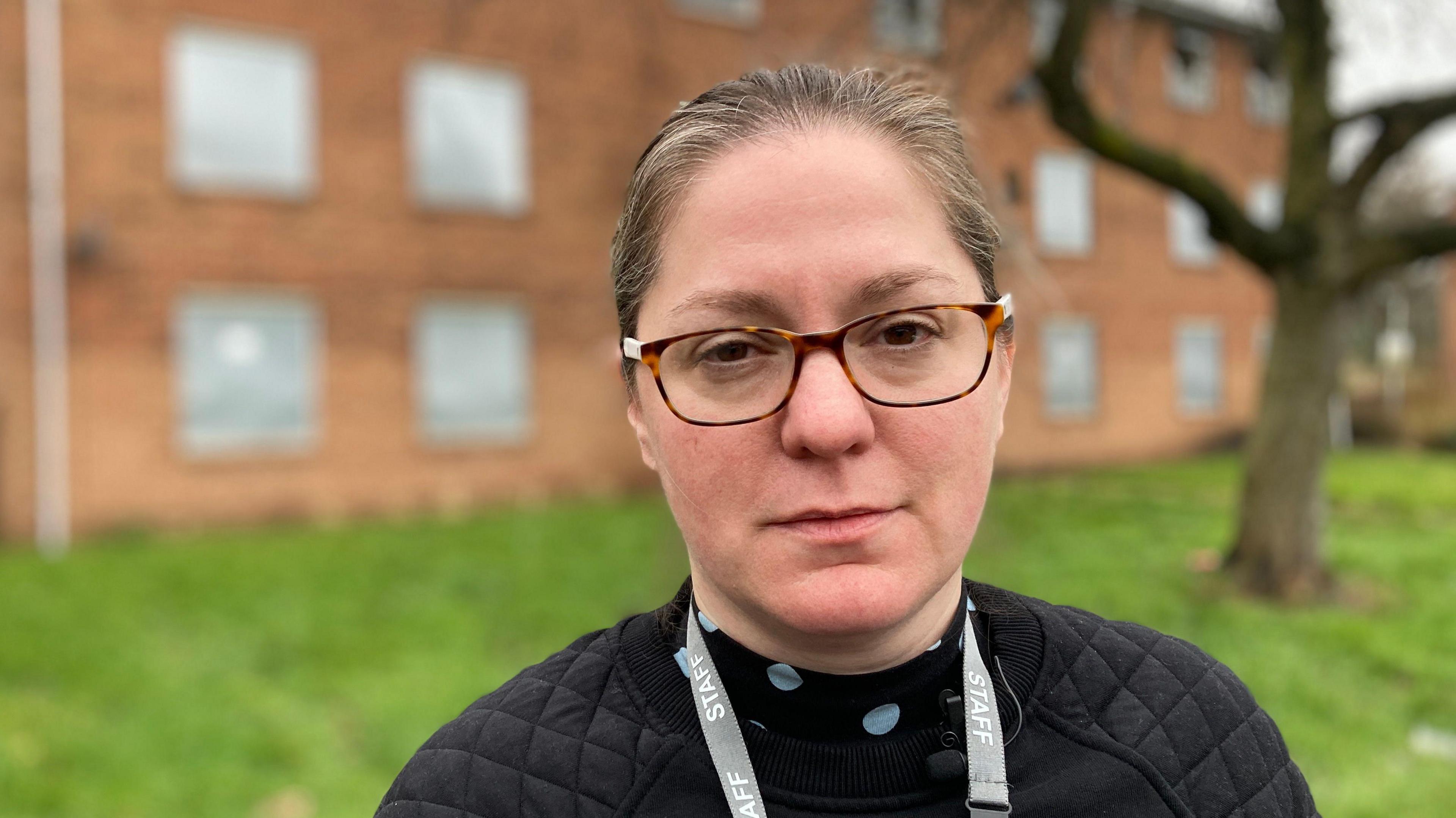 Tor Berry is the Development Manager at the Leicester branch of the brain injury charity Headway. Their centre is at the end of Hospital Close. She is wearing glasses and looking directly into camera. In the background you can see properties on Hospital Close with metal shutters over the windows. 