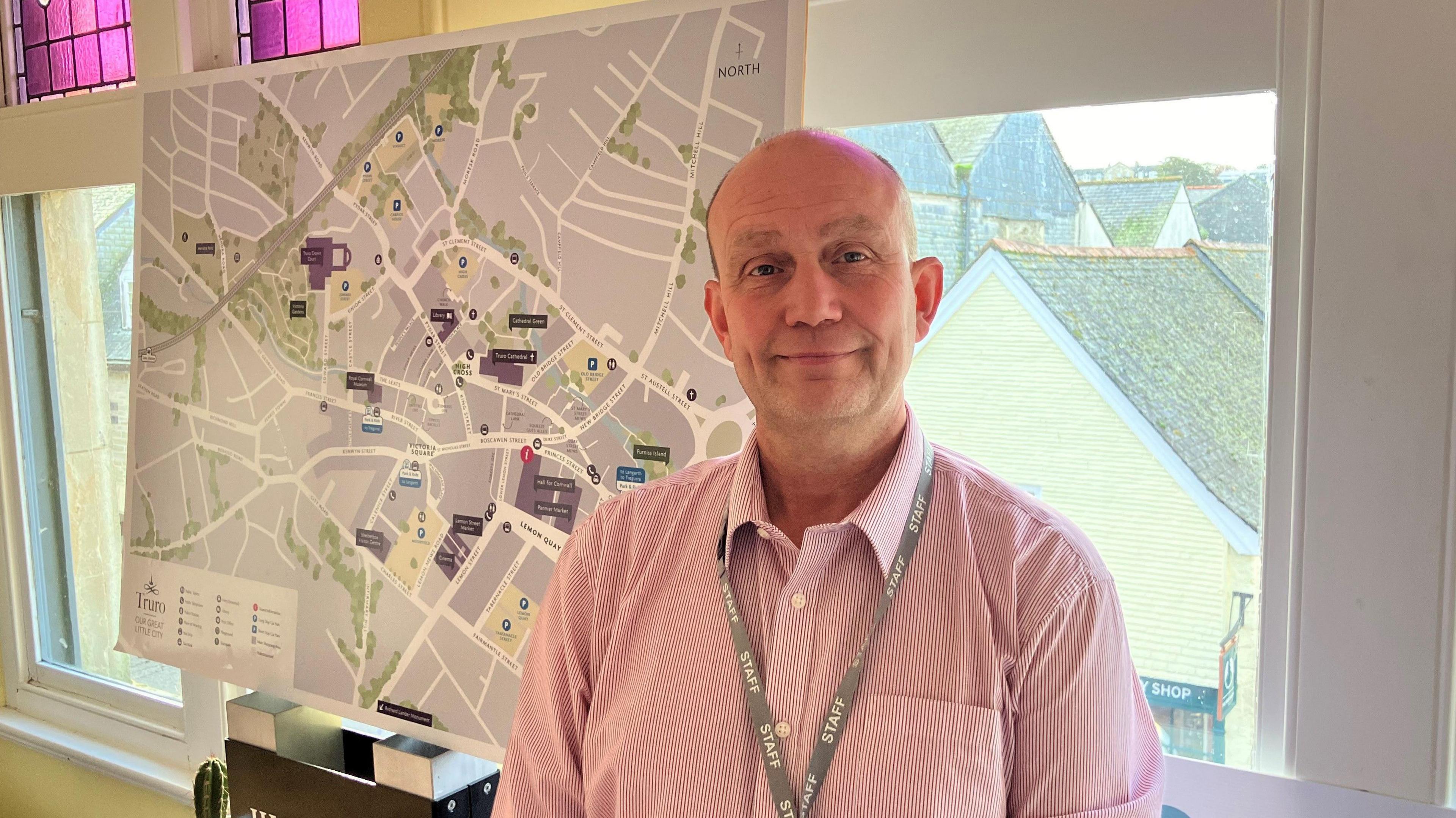 Alun Jones from Truro Business Improvement District , in a red and white striped shirt, smiling in a room standing in front of a window