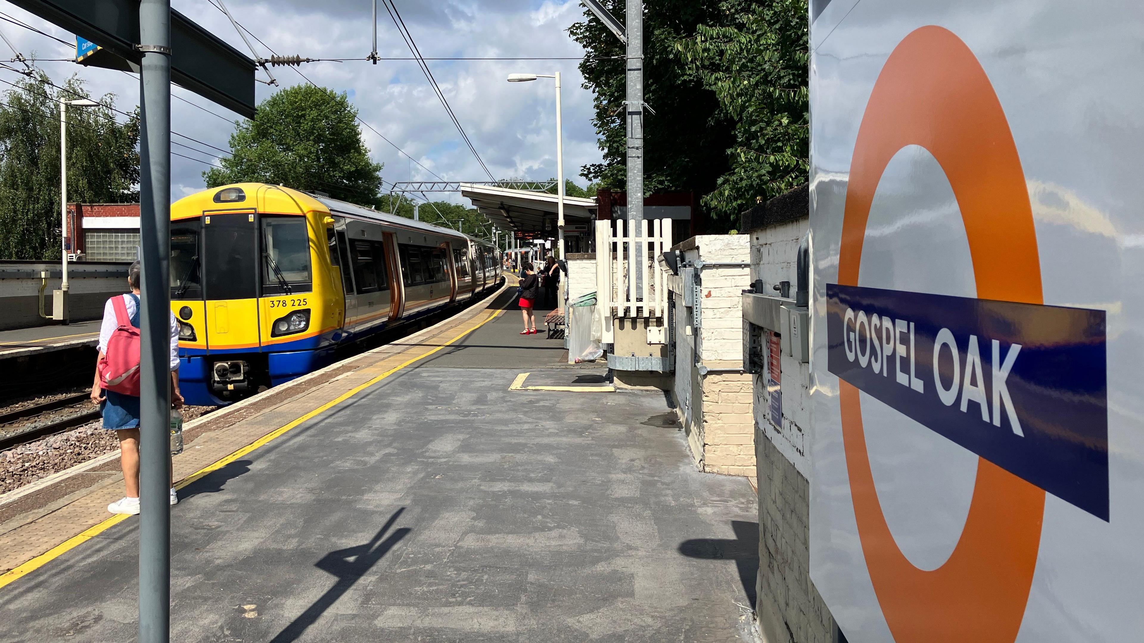 Orange Overground roundel at Gospel Oak overground station as a yellow-fronted train arrives on the platform