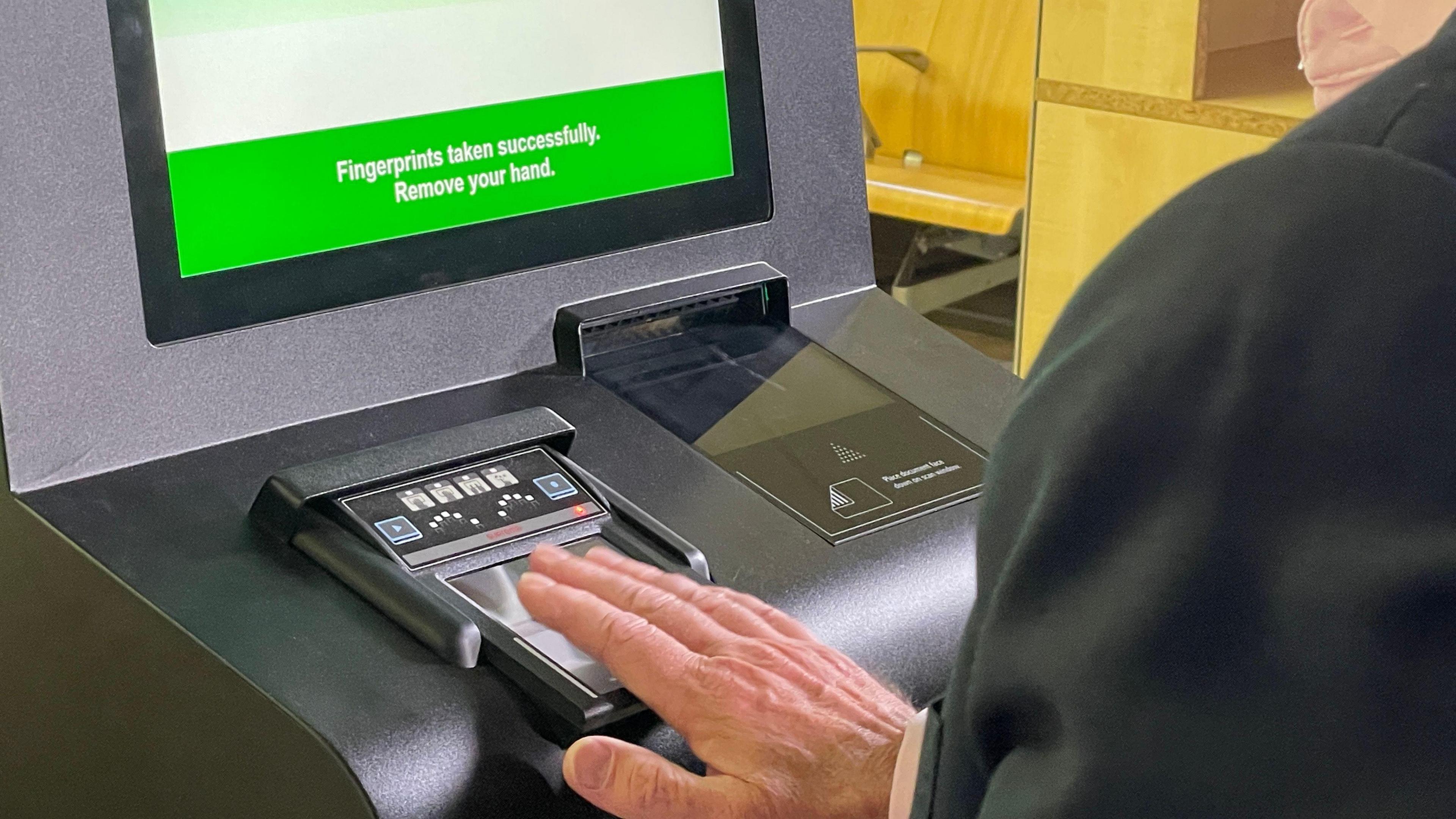 A male passenger having his fingerprints taken by a scanner.